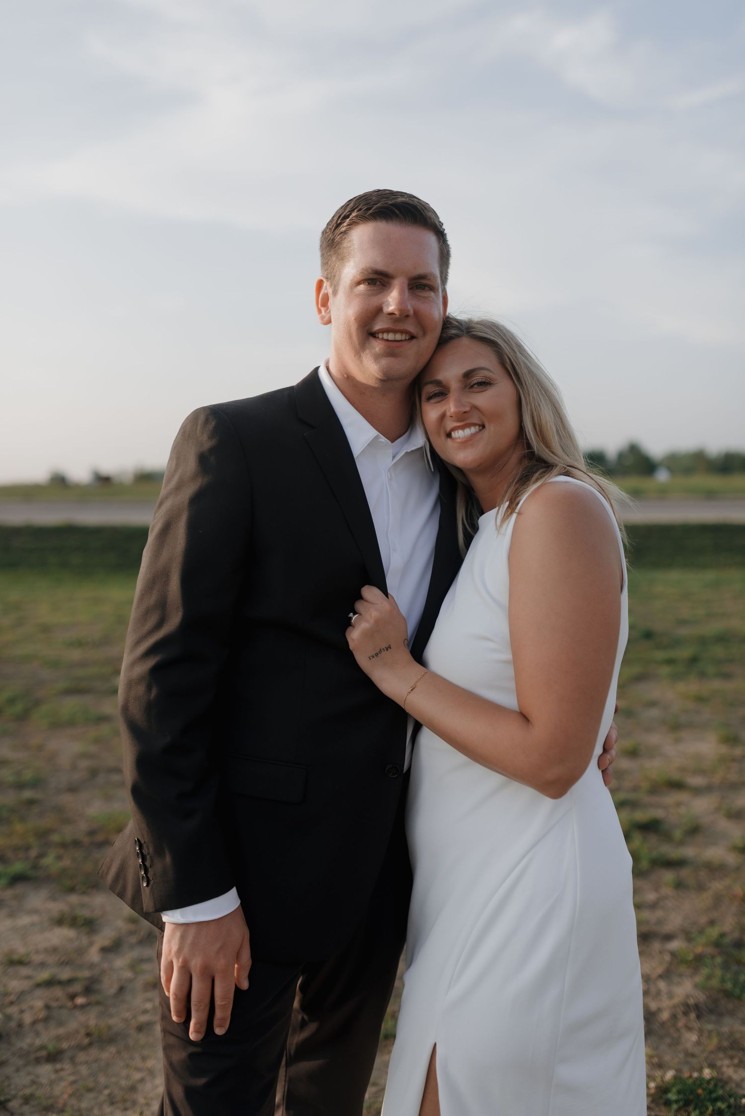 Joyful couple embraces outdoors at golden hour, bride in white dress and groom in dark suit smiling.