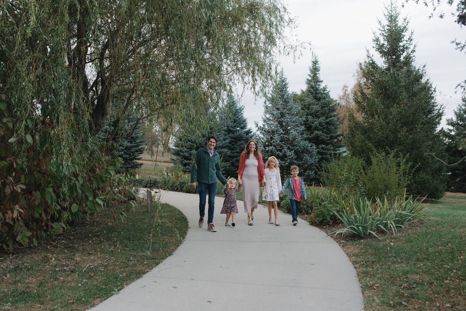 A family of four strolls together on a winding park path surrounded by greenery.