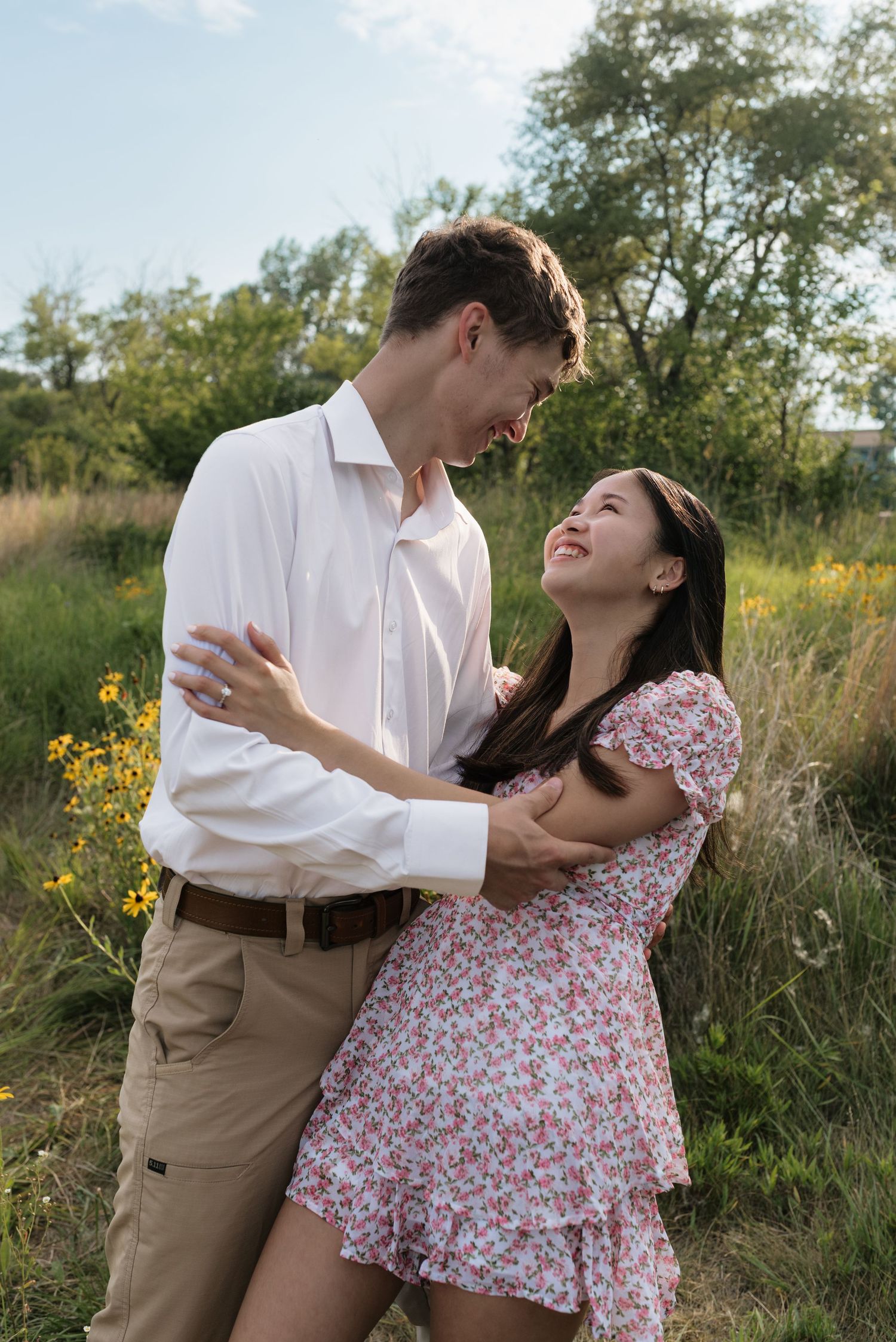 Happy couple embracing and smiling at each other in a sunny wildflower meadow.