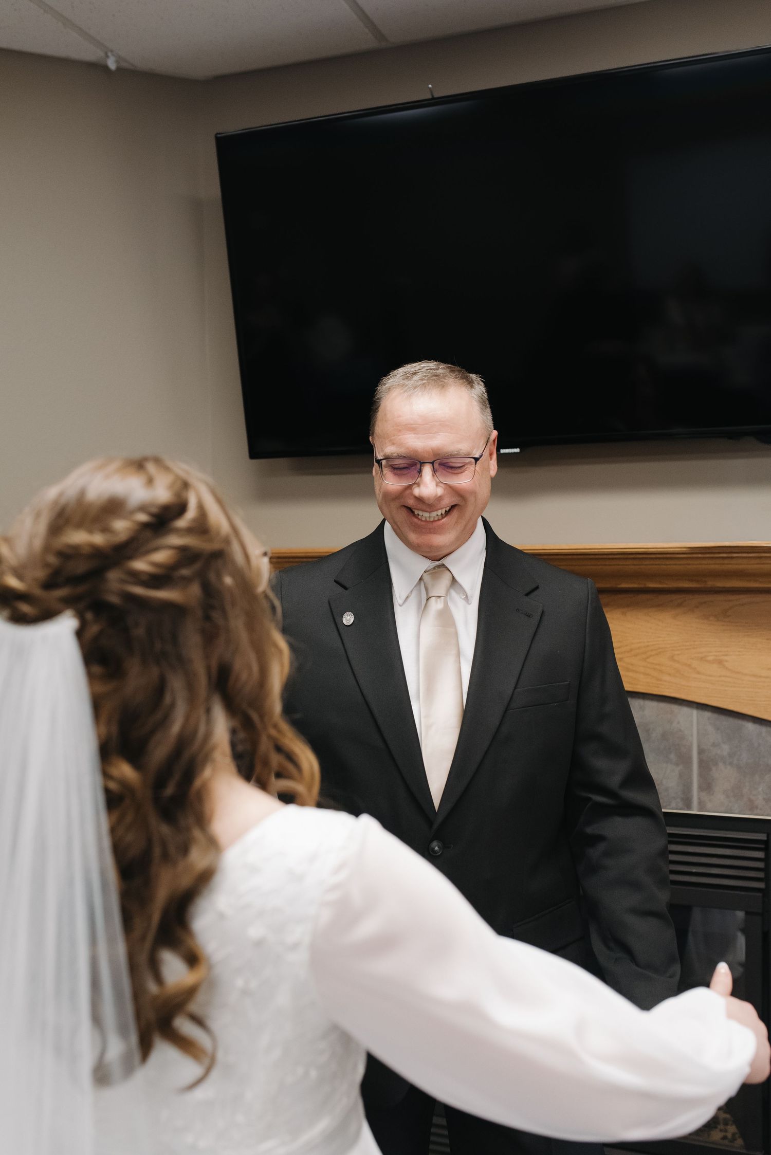 Smiling father in black suit reacts emotionally seeing his daughter in wedding dress during first look moment.