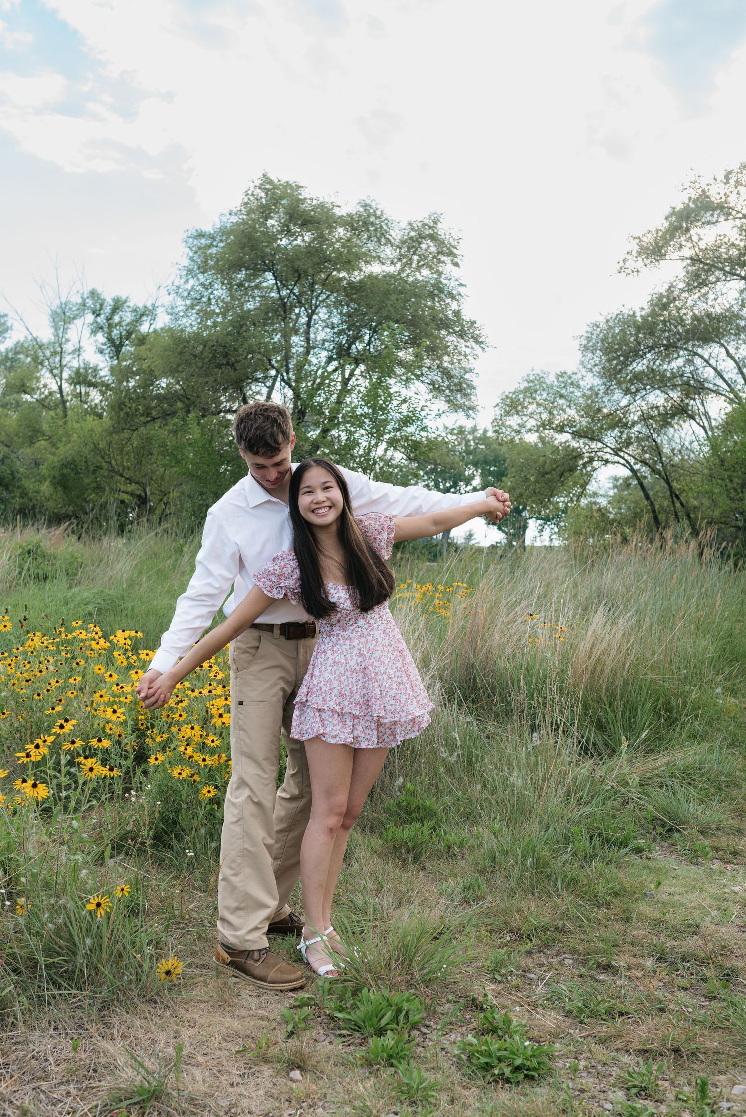 Happy couple dancing among yellow wildflowers in a lush green meadow during an engagement session.