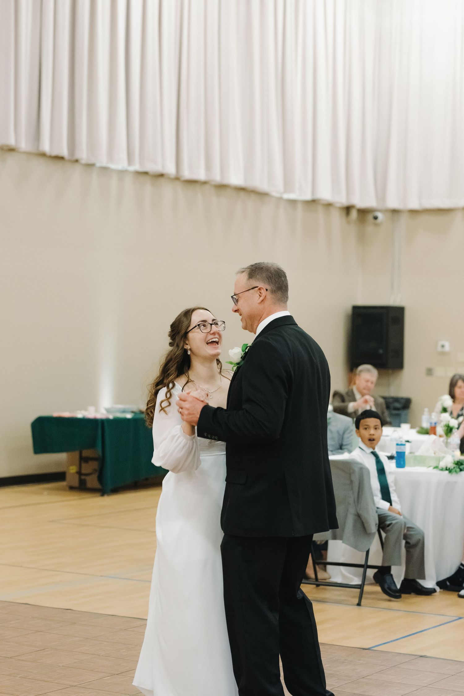Bride laughing joyfully while sharing a father-daughter dance at her wedding reception.
