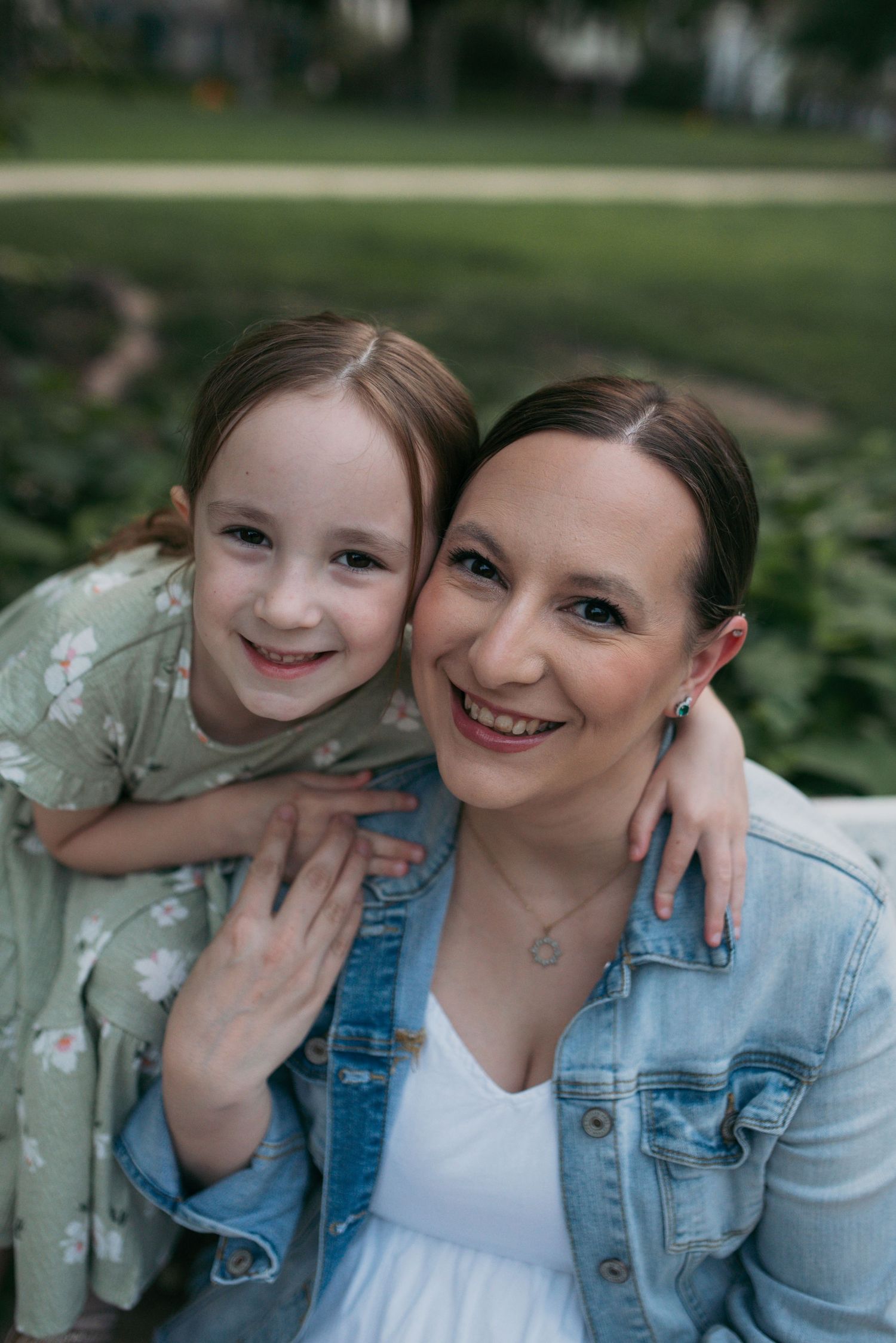 Loving mother and daughter in matching green tones smiling together outdoors in a park.