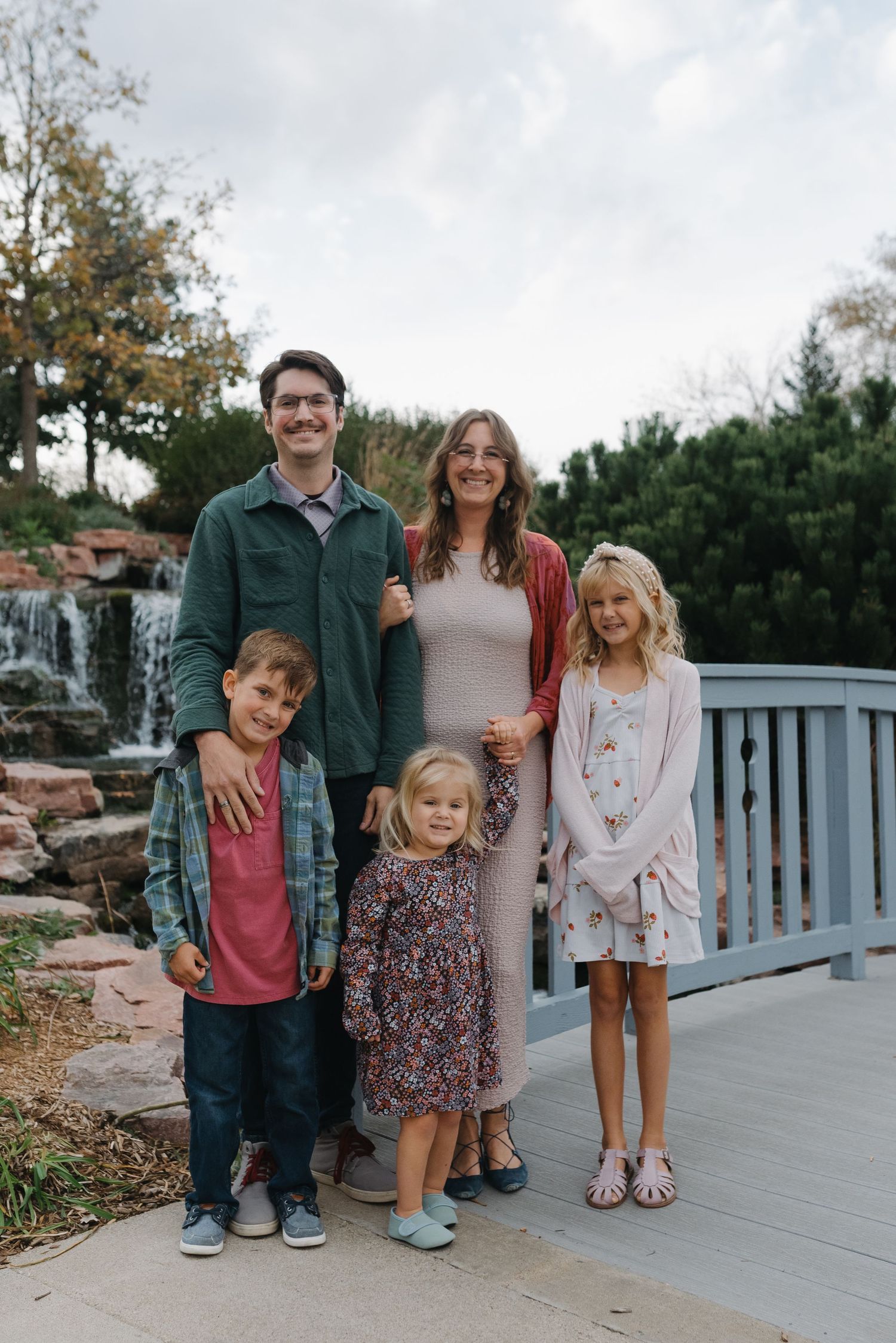 Happy family of five posing on bridge with waterfall backdrop in autumn park.