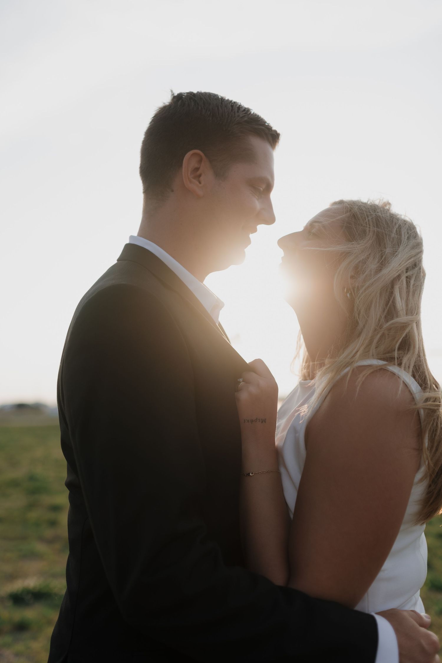 Romantic backlit silhouette of bride and groom embracing at sunset with golden light glowing between them.