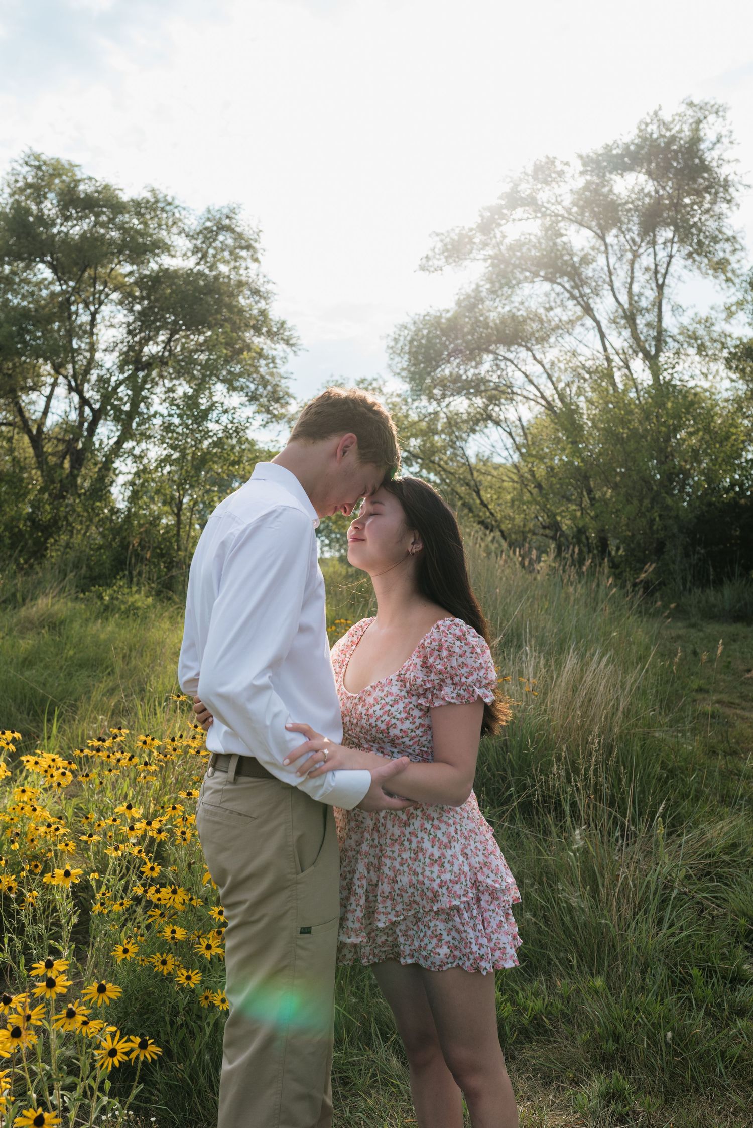 Romantic couple holding hands and touching foreheads near yellow wildflowers in a field.