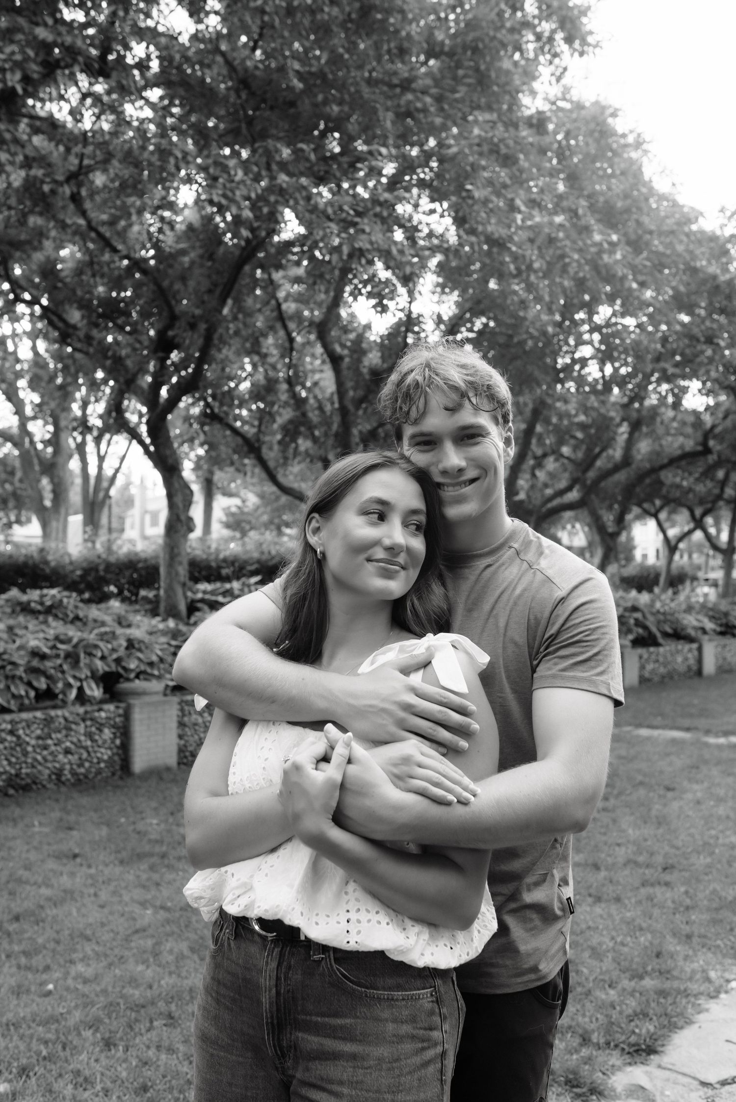 Young couple embracing in a park, smiling warmly in a black and white outdoor portrait photo.