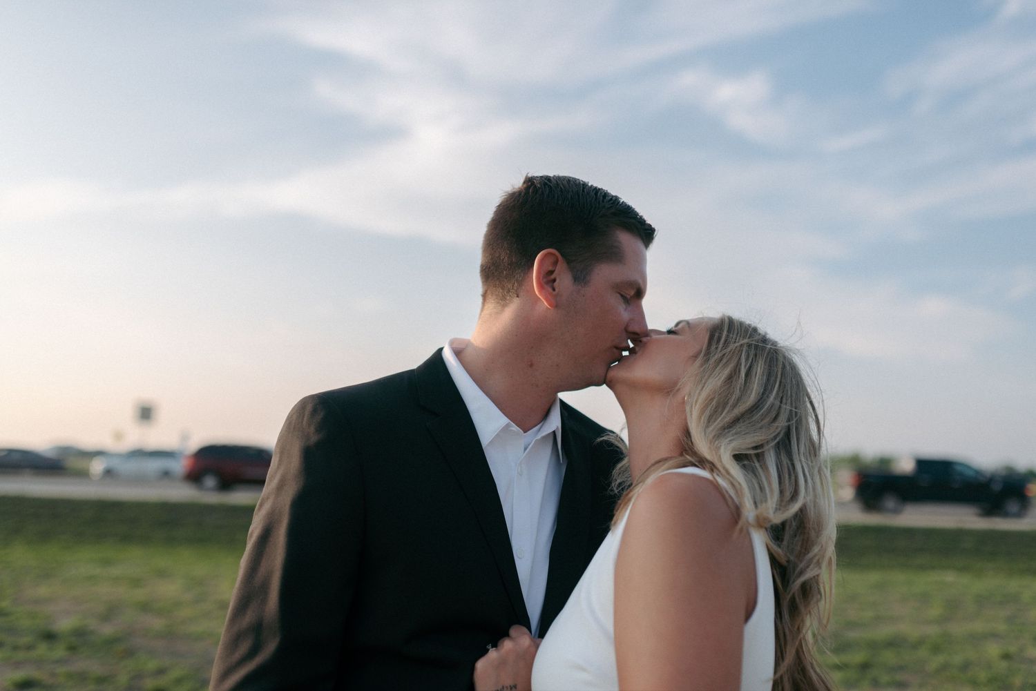 Bride and groom sharing a romantic kiss outdoors under a blue sky at golden hour.