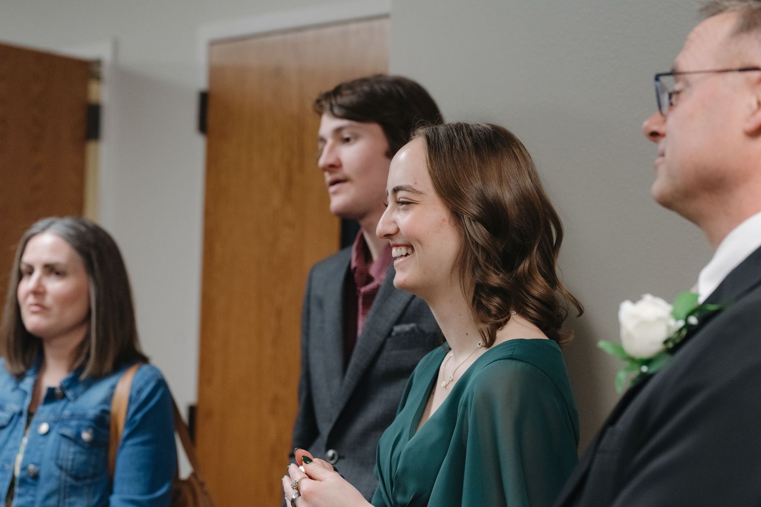 A woman in a green dress laughs joyfully during a wedding ceremony beside a man in a suit.