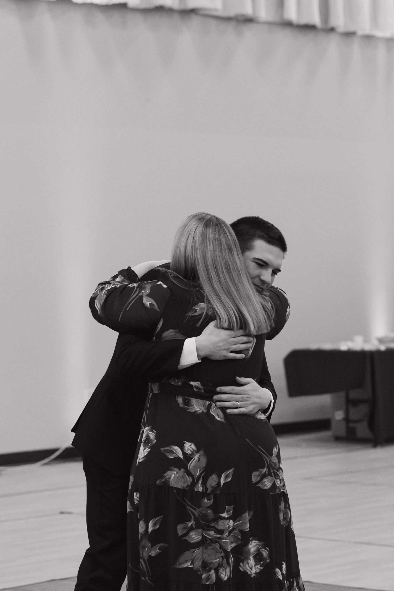 Black and white photo of a couple sharing a tender embrace while dancing at a formal event.