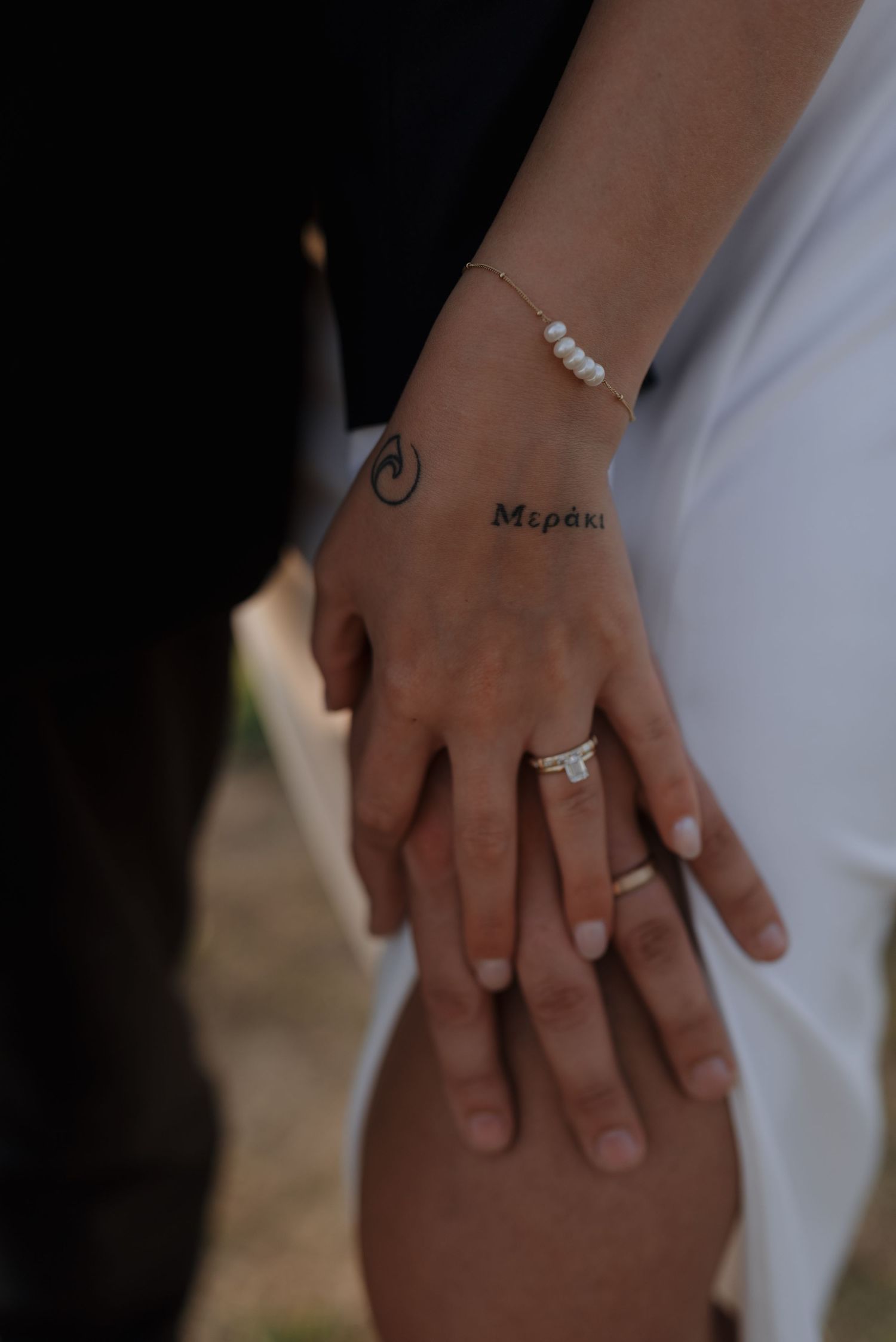 Detail shot of newlyweds hands with wedding rings, a Meraki tattoo, and a delicate pearl bracelet.