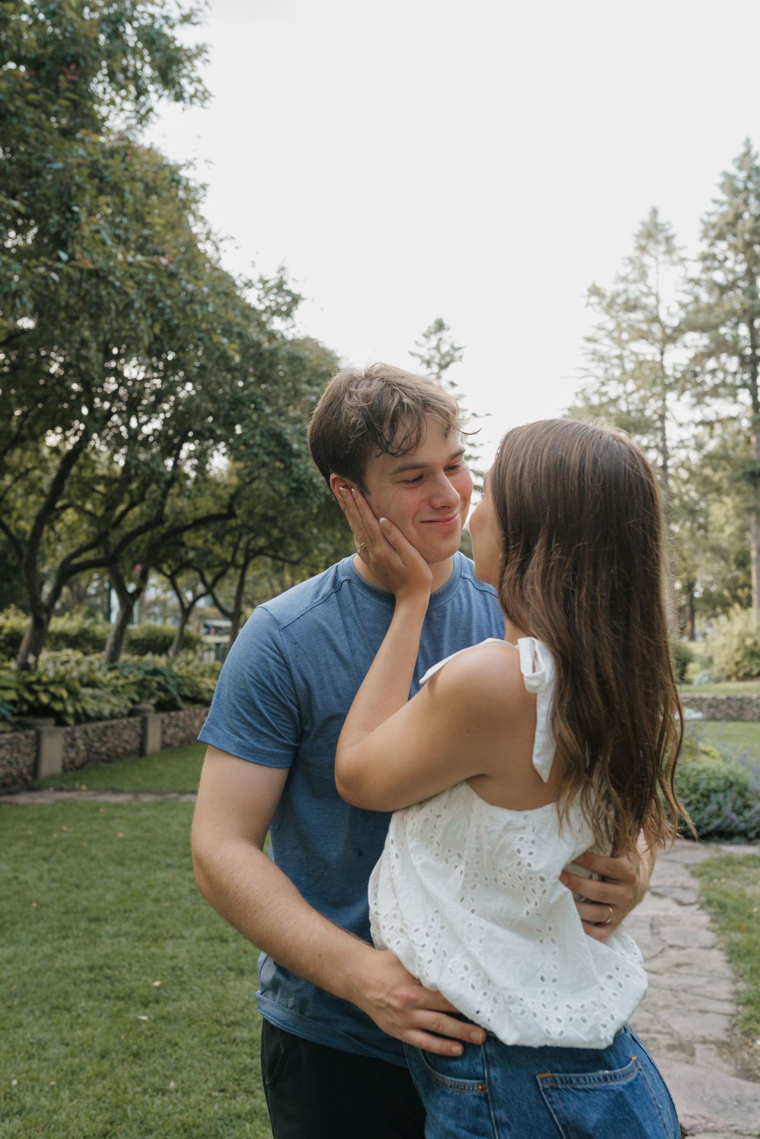A young couple sharing a tender moment in a lush green park, with the woman gently touching the man's face.