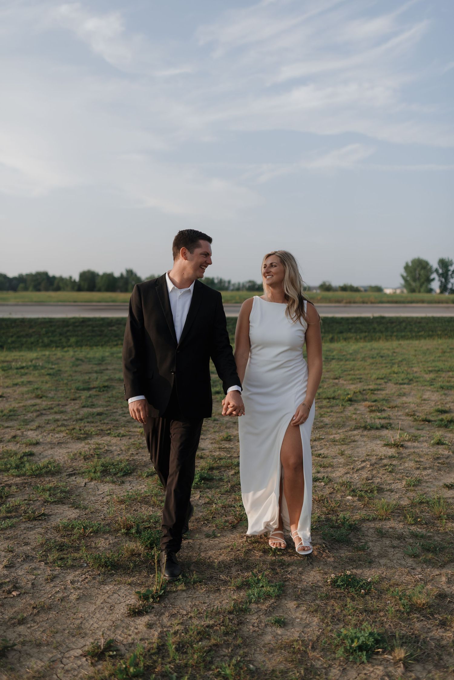 Happy newlyweds in wedding attire walking and laughing together in an open outdoor setting.