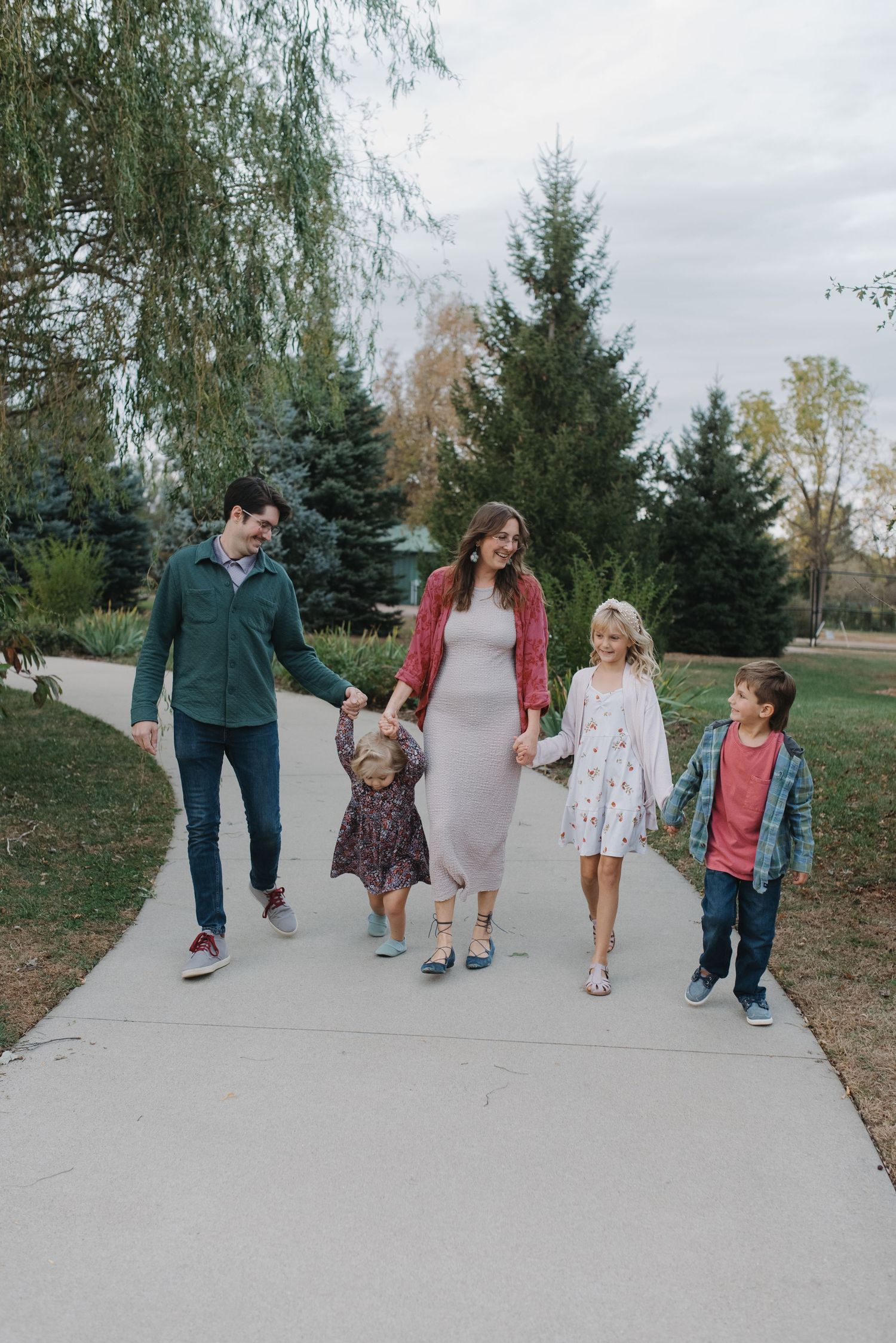 Family of five holding hands while walking on a park path on a cloudy day.