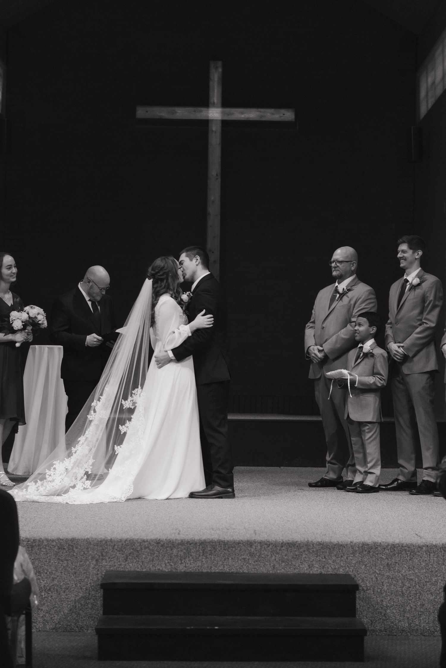 Bride and groom share first kiss at church altar during wedding ceremony in black and white.