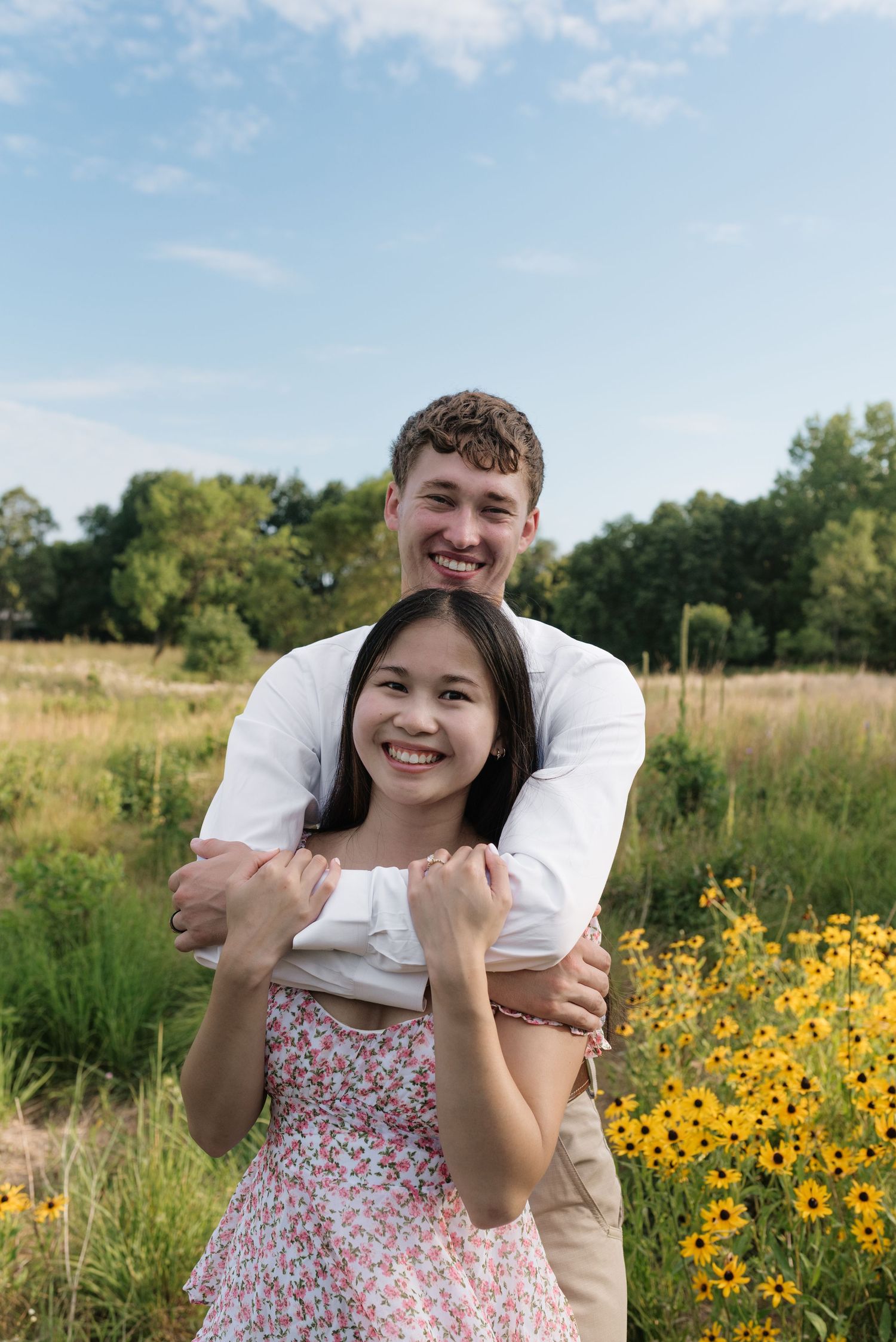 Happy couple embracing near yellow wildflowers in a lush green field on a sunny day.