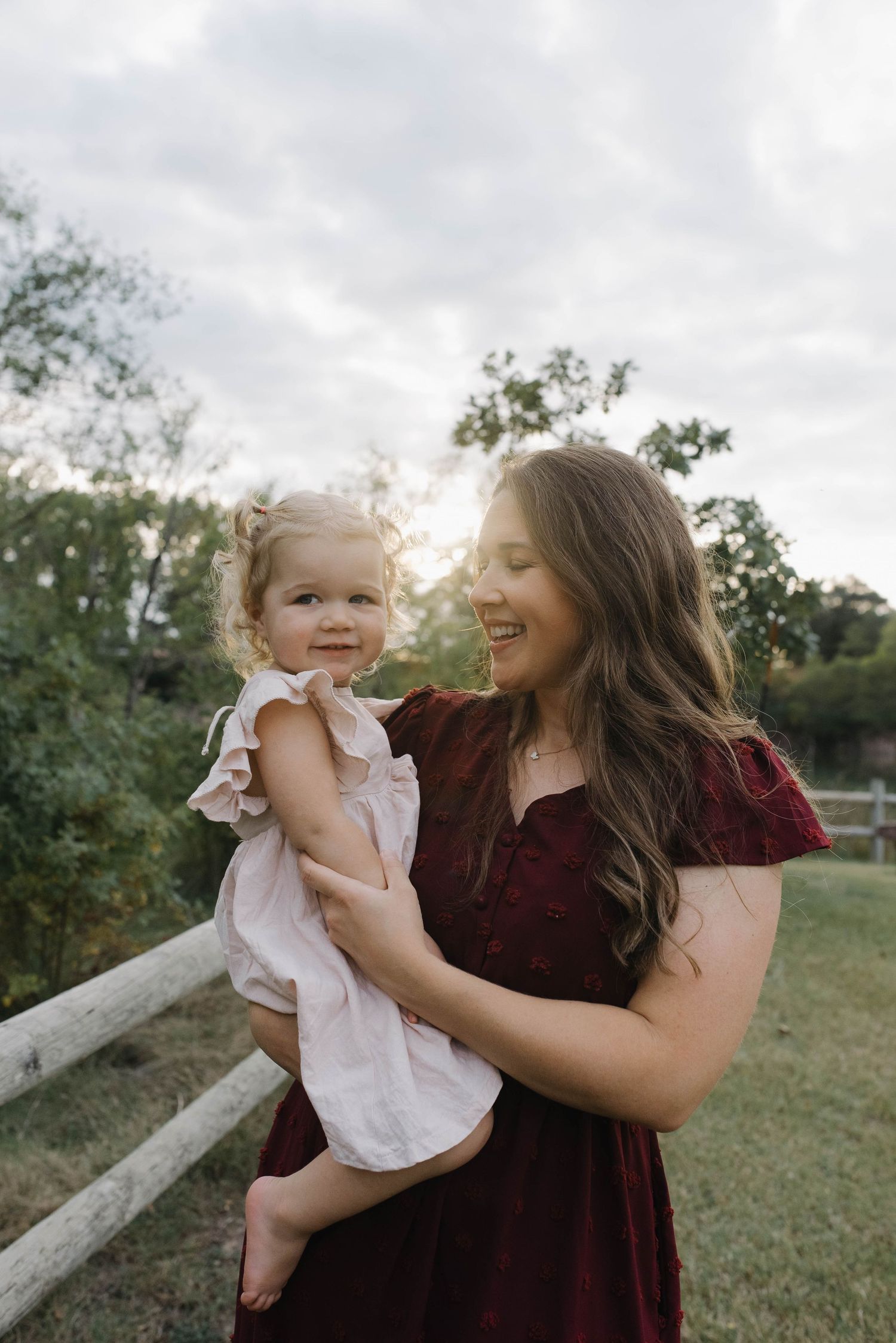 Smiling mother in a red dress holding her happy toddler daughter during an outdoor portrait session at golden hour.
