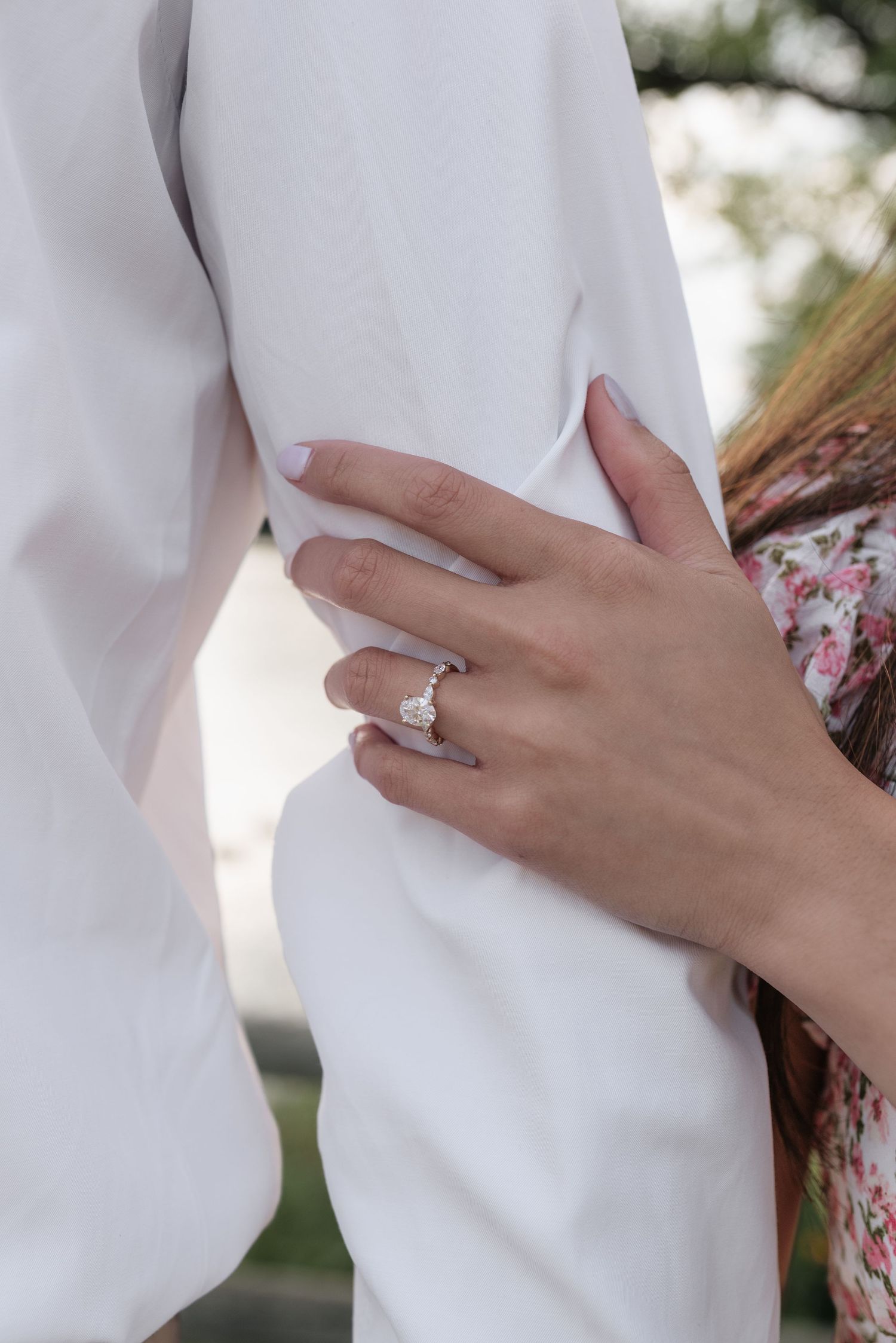 Close-up of an engagement ring on a woman's hand as she embraces a man in a white shirt.
