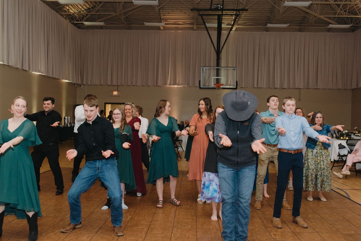 Wedding guests line dancing together in green dresses and casual attire at a festive reception.