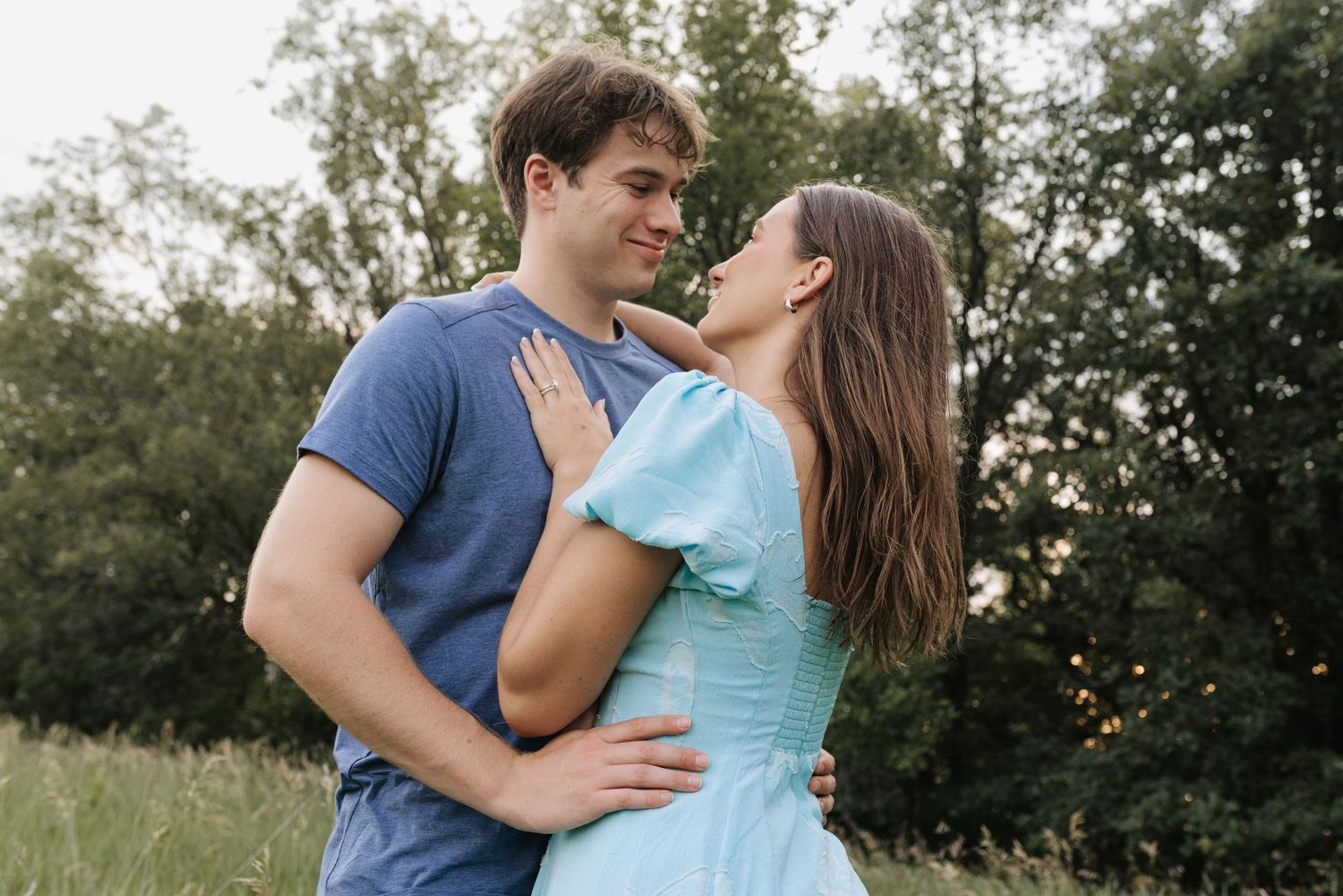 Couple sharing a romantic moment outdoors in a green field, woman in blue dress and man in navy shirt embracing.