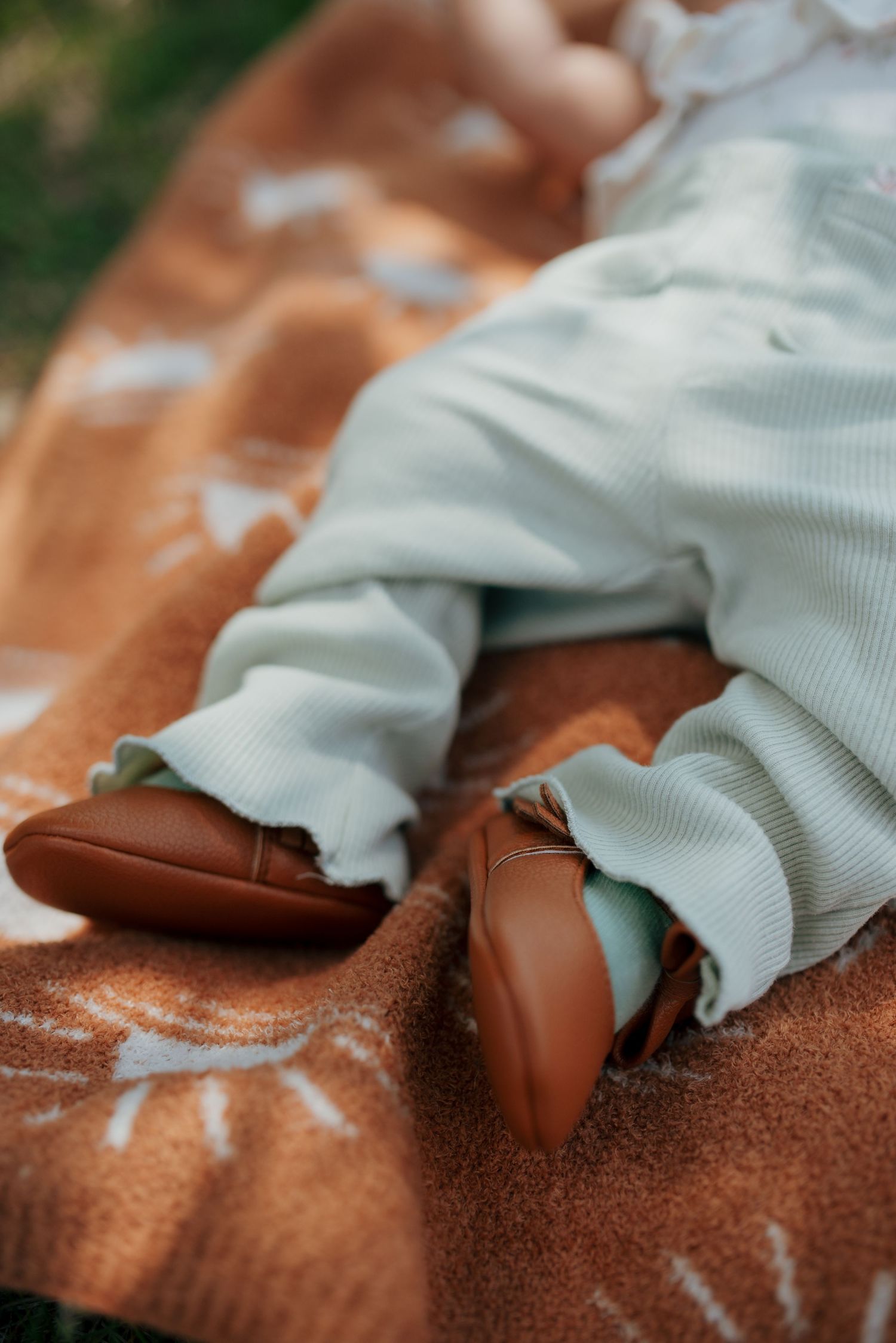 Close-up of baby wearing mint outfit and brown leather shoes on a sunprint blanket.