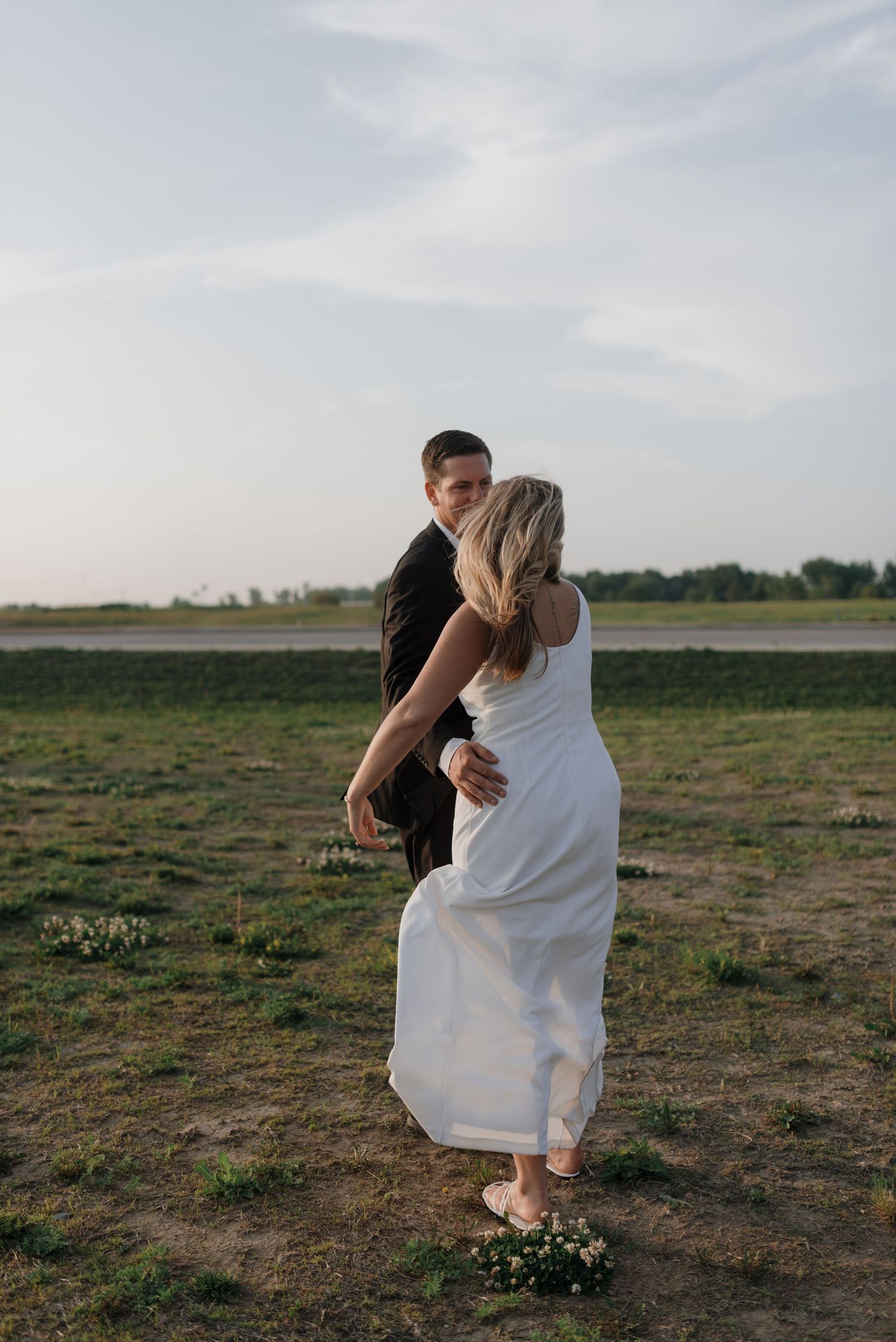 Bride and groom share a romantic embrace in an open field during wedding portraits.