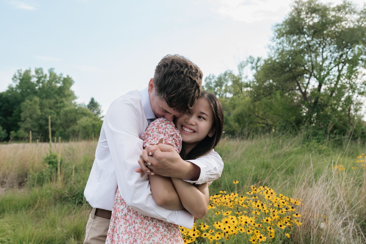 A couple sharing a tender embrace among tall grasses and bright yellow wildflowers outdoors.