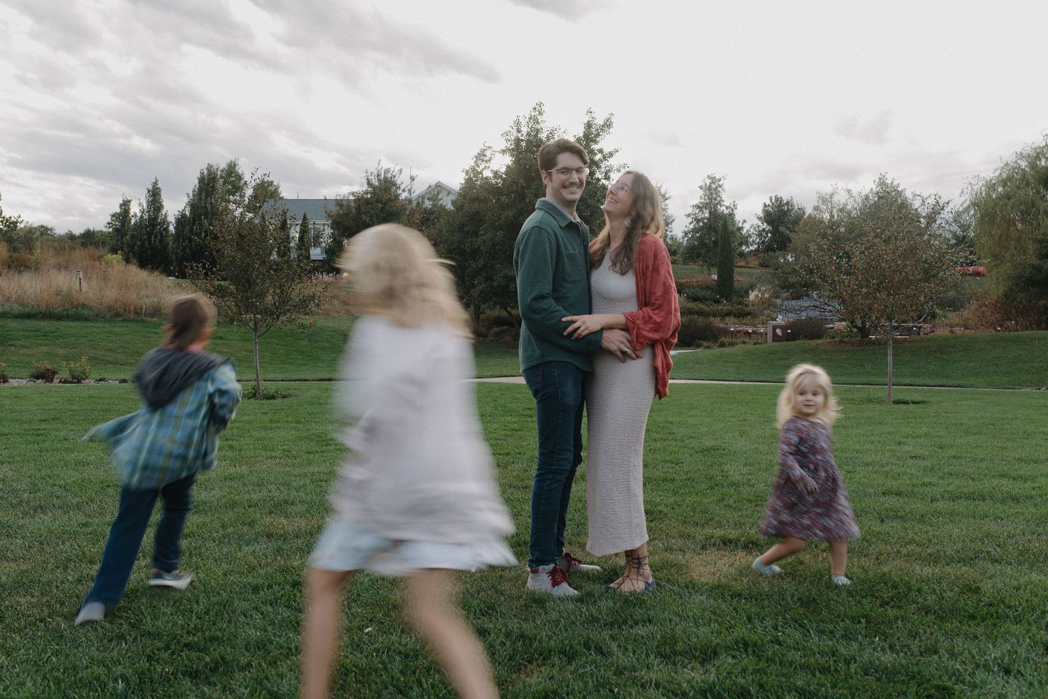 Couple embracing on green grass while children move around them in a park.
