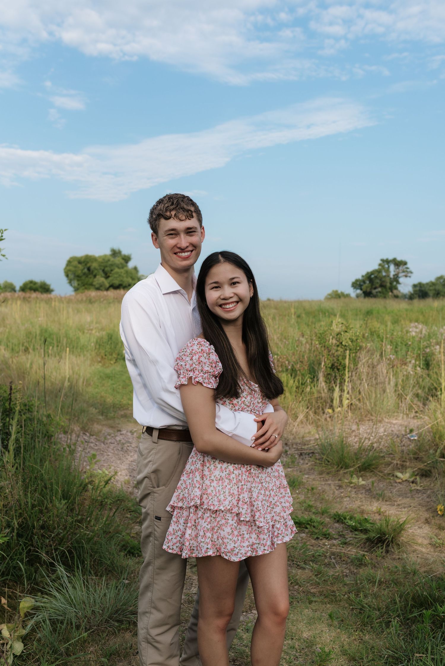 Smiling couple posing together in a sunny green meadow, woman in floral dress.