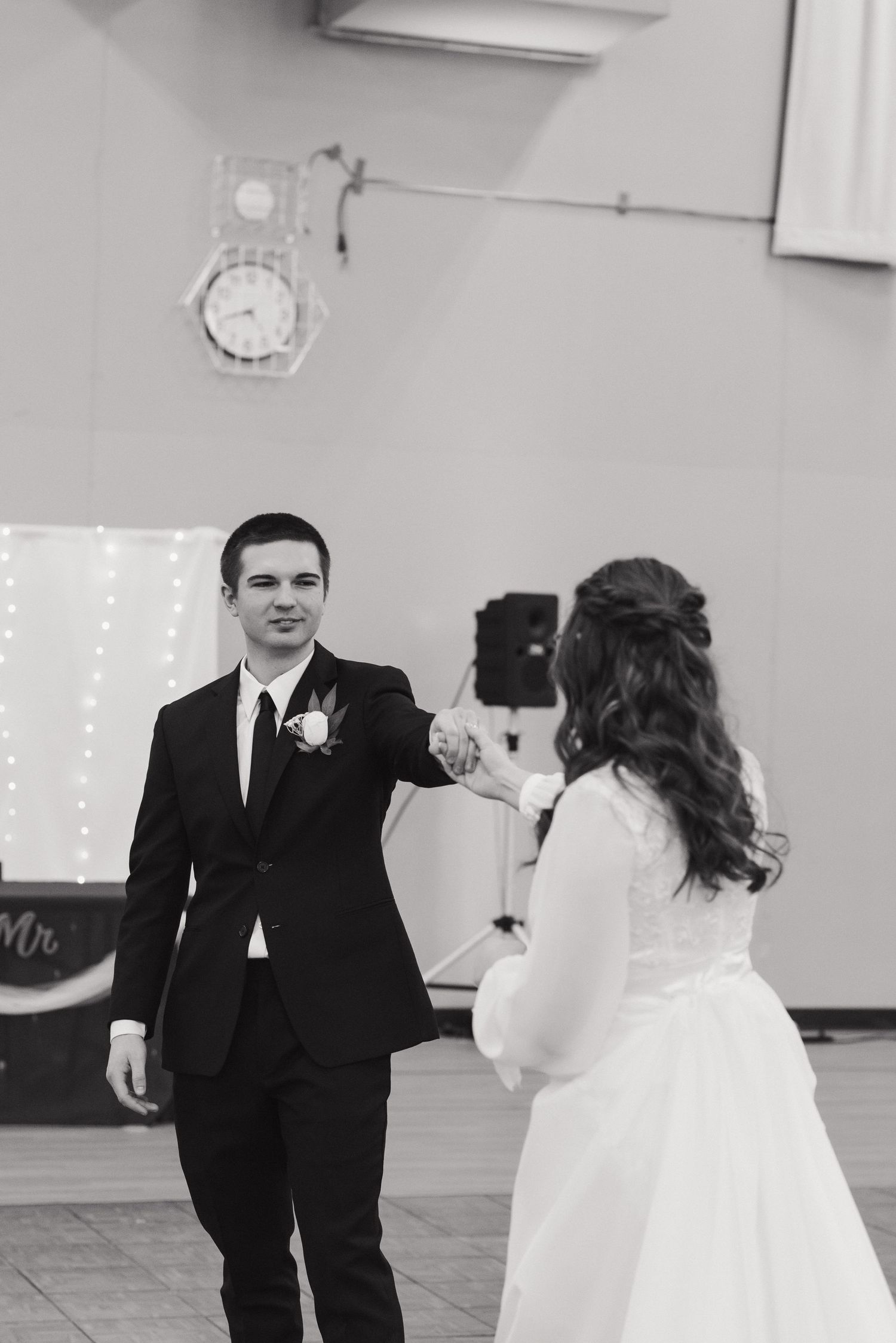 Black and white photo of bride and groom holding hands during their first dance at wedding reception.