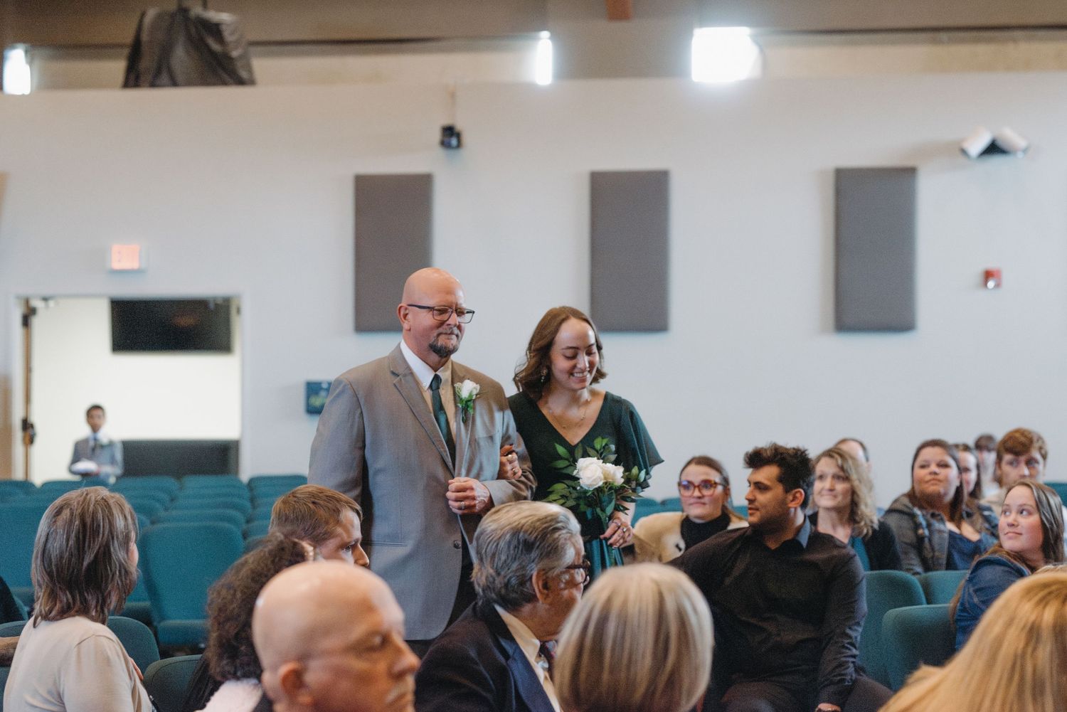 A smiling couple walks down the aisle at a wedding ceremony in a modern church venue.