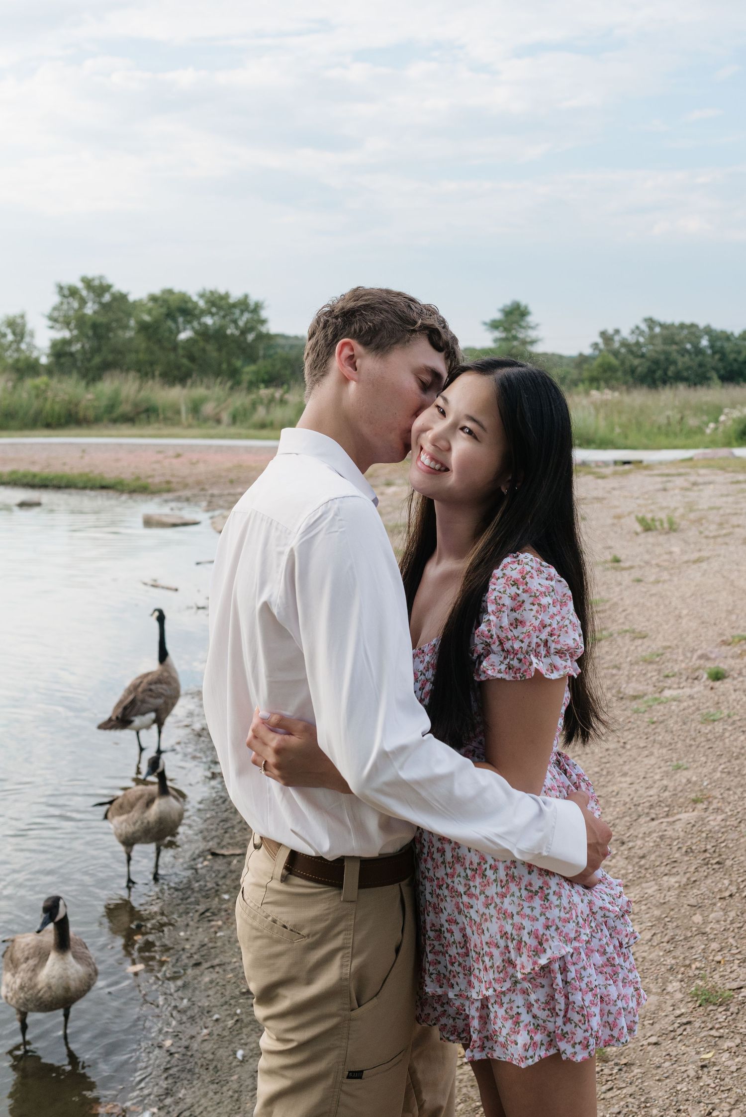 Couple sharing a kiss near a lakeside with Canada geese in the background during engagement shoot.
