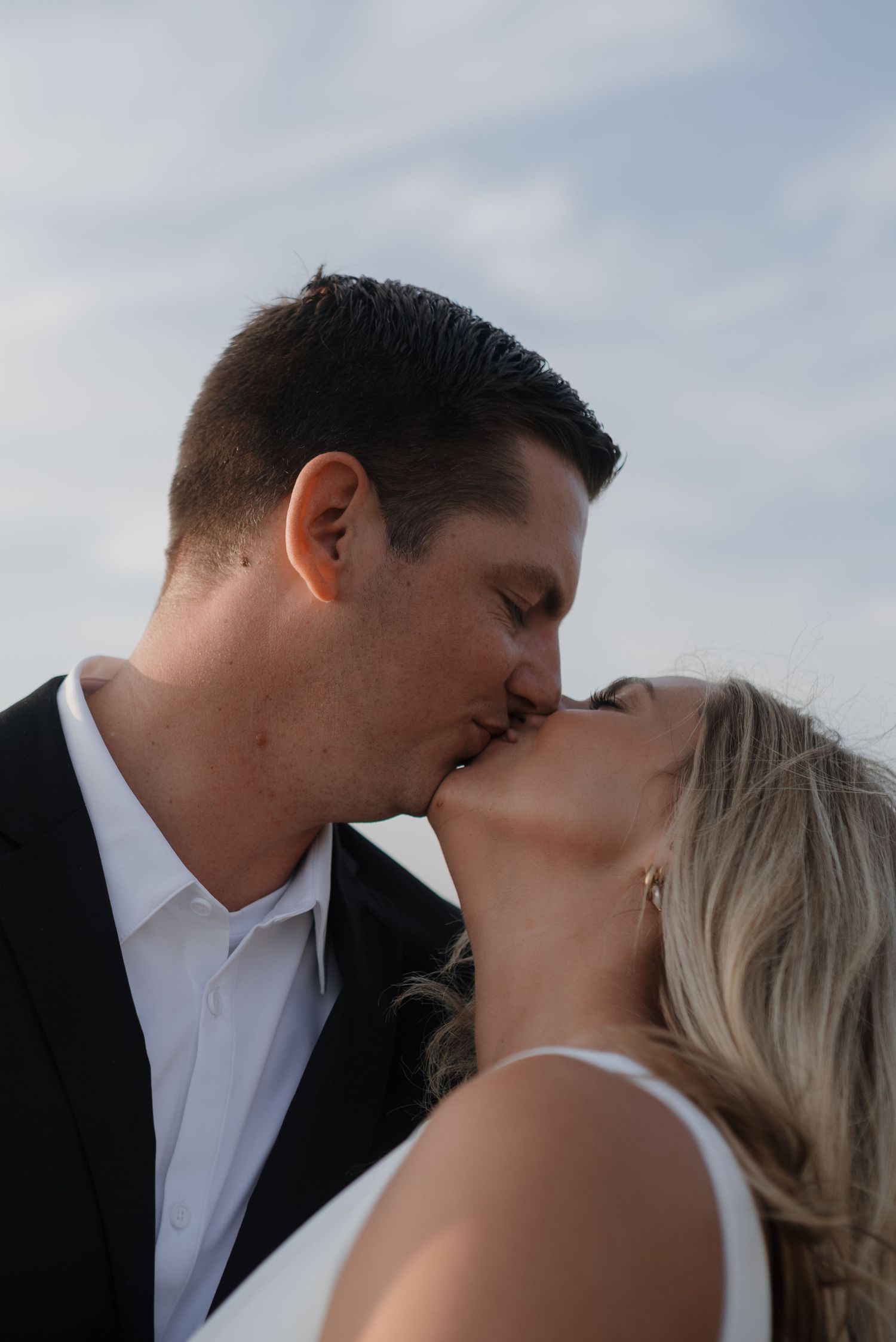 Intimate portrait of a bride and groom kissing against a bright blue sky background.