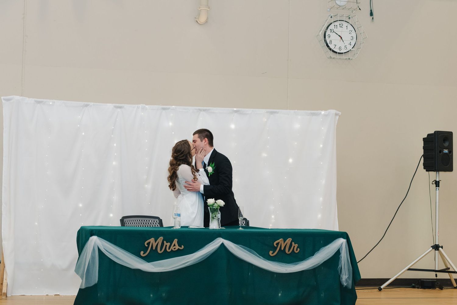 Bride and groom kissing at sweetheart table decorated with Mrs. and Mr. signs at wedding reception.