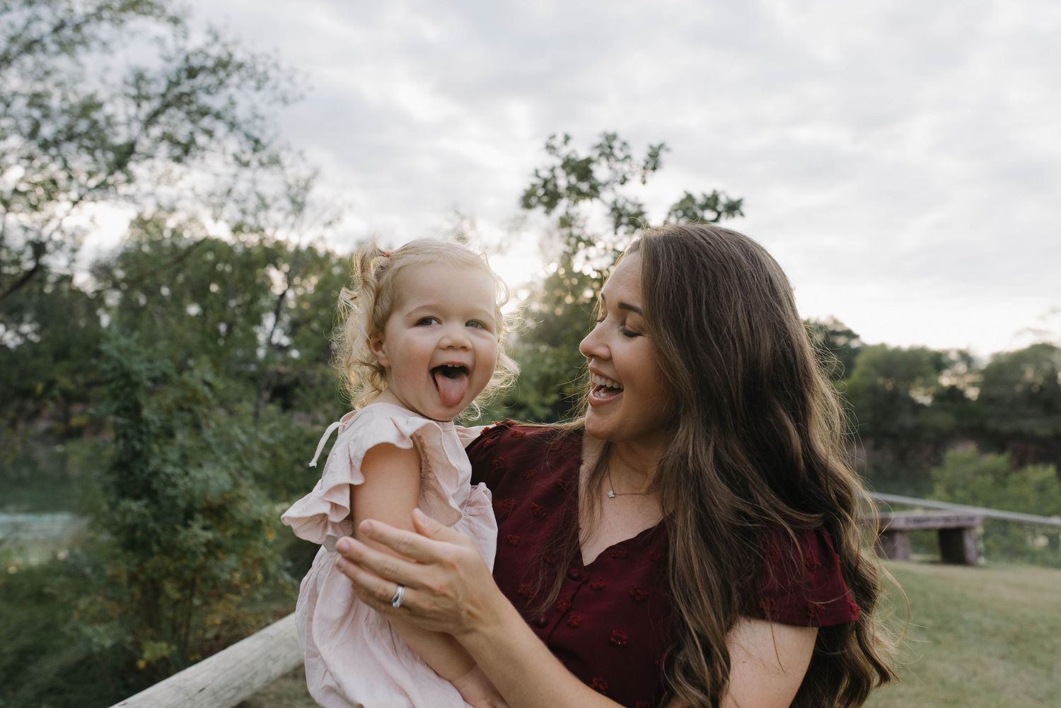 Laughing mother and toddler daughter sharing a joyful moment together during an outdoor photo session at sunset.