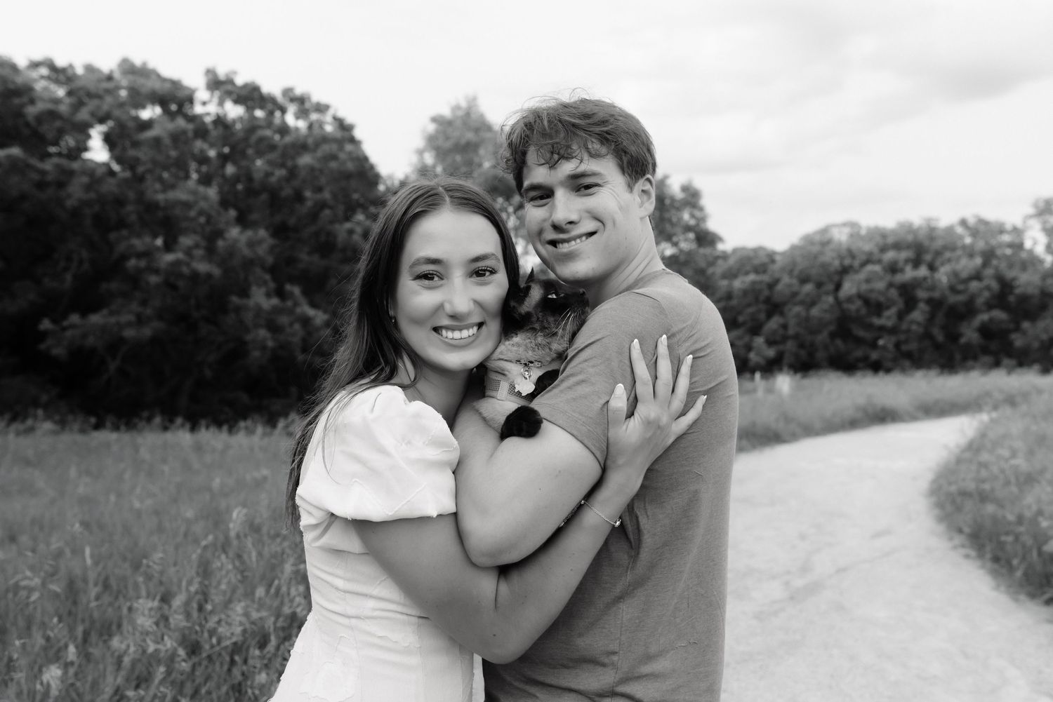 Smiling couple embracing outdoors in a field, black and white romantic portrait photo.