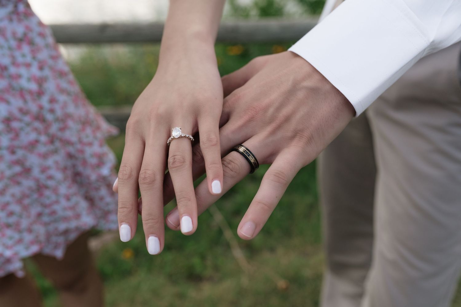 Couple displaying wedding rings, woman wearing diamond engagement ring with white nails, man wearing black band ring.