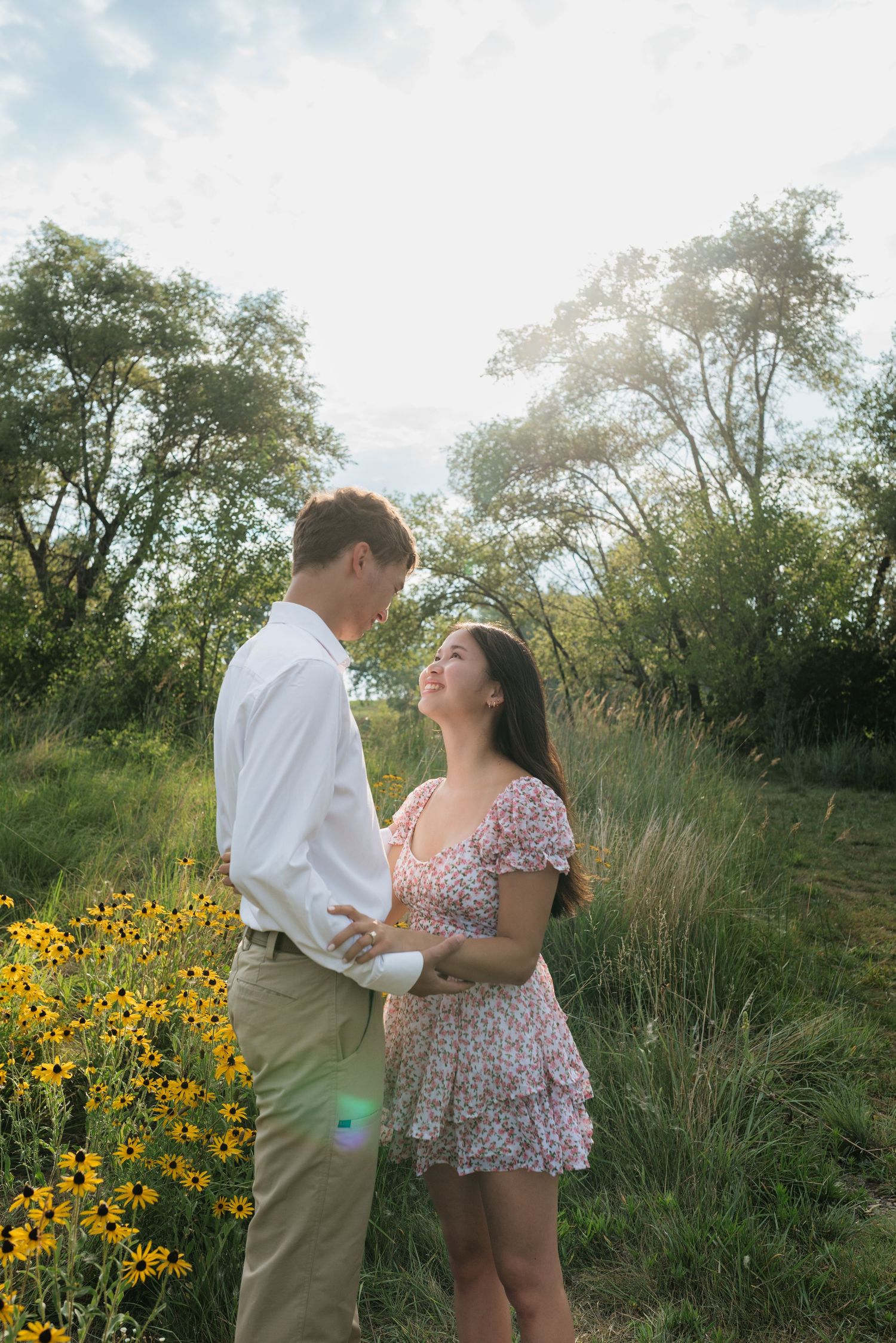 Couple holding hands and gazing at each other beside yellow wildflowers in a sunlit meadow.