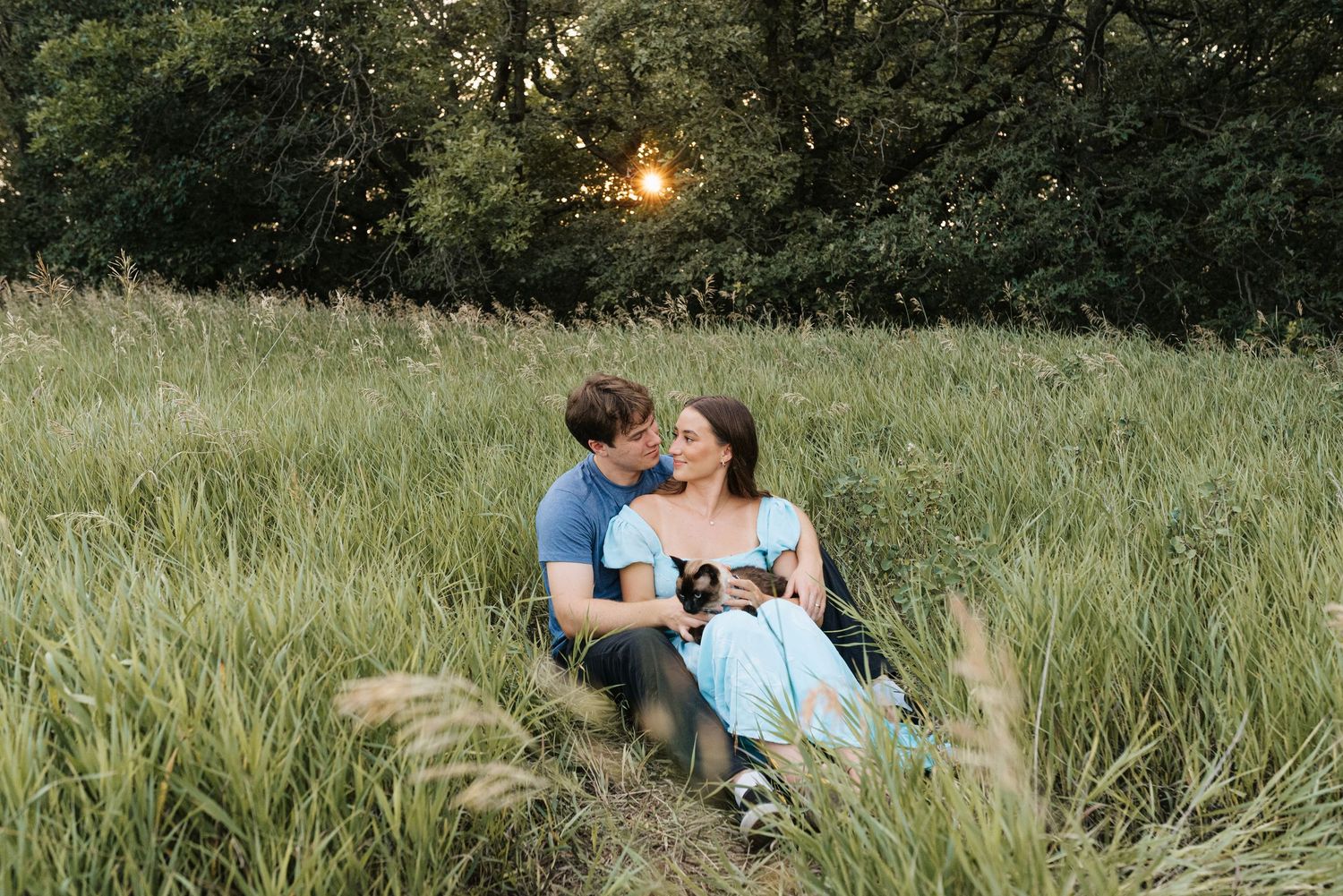 Couple sitting together in a lush green meadow at sunset, sharing a romantic moment outdoors.