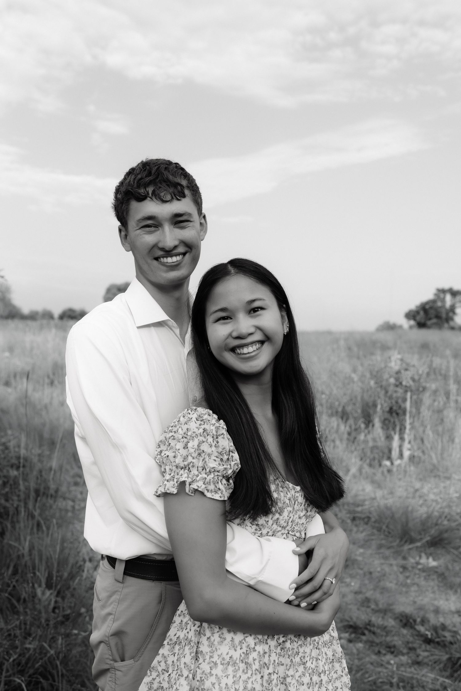 Black and white portrait of a joyful couple embracing in a wide open field during golden hour.