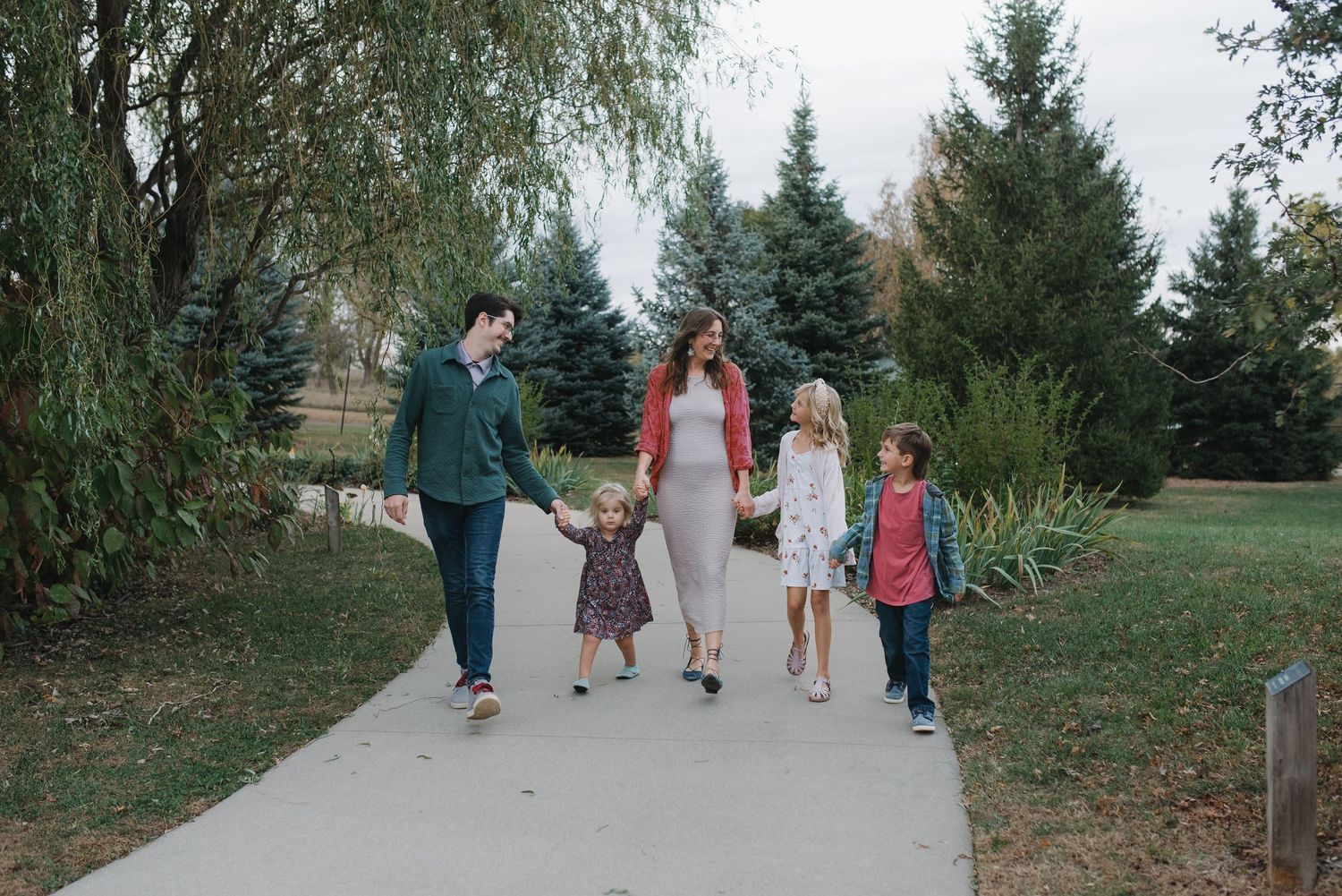Smiling family walking together on a paved park path among green trees.
