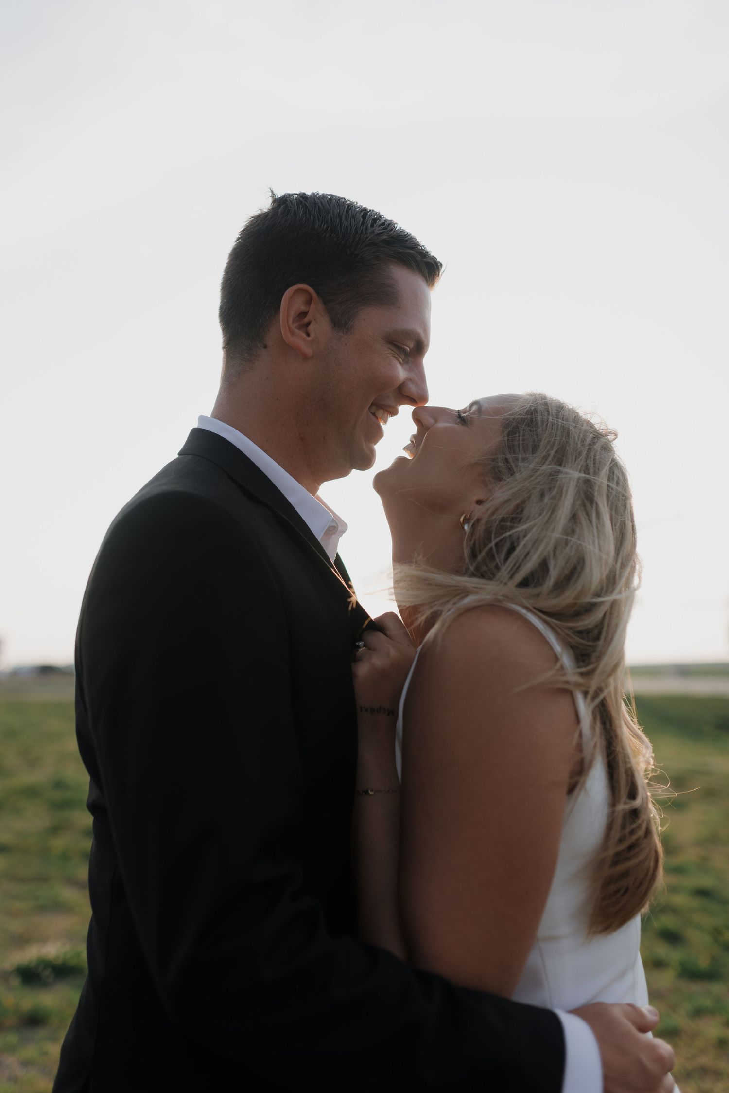 Joyful bride and groom sharing an intimate moment, nearly kissing outdoors at golden hour.