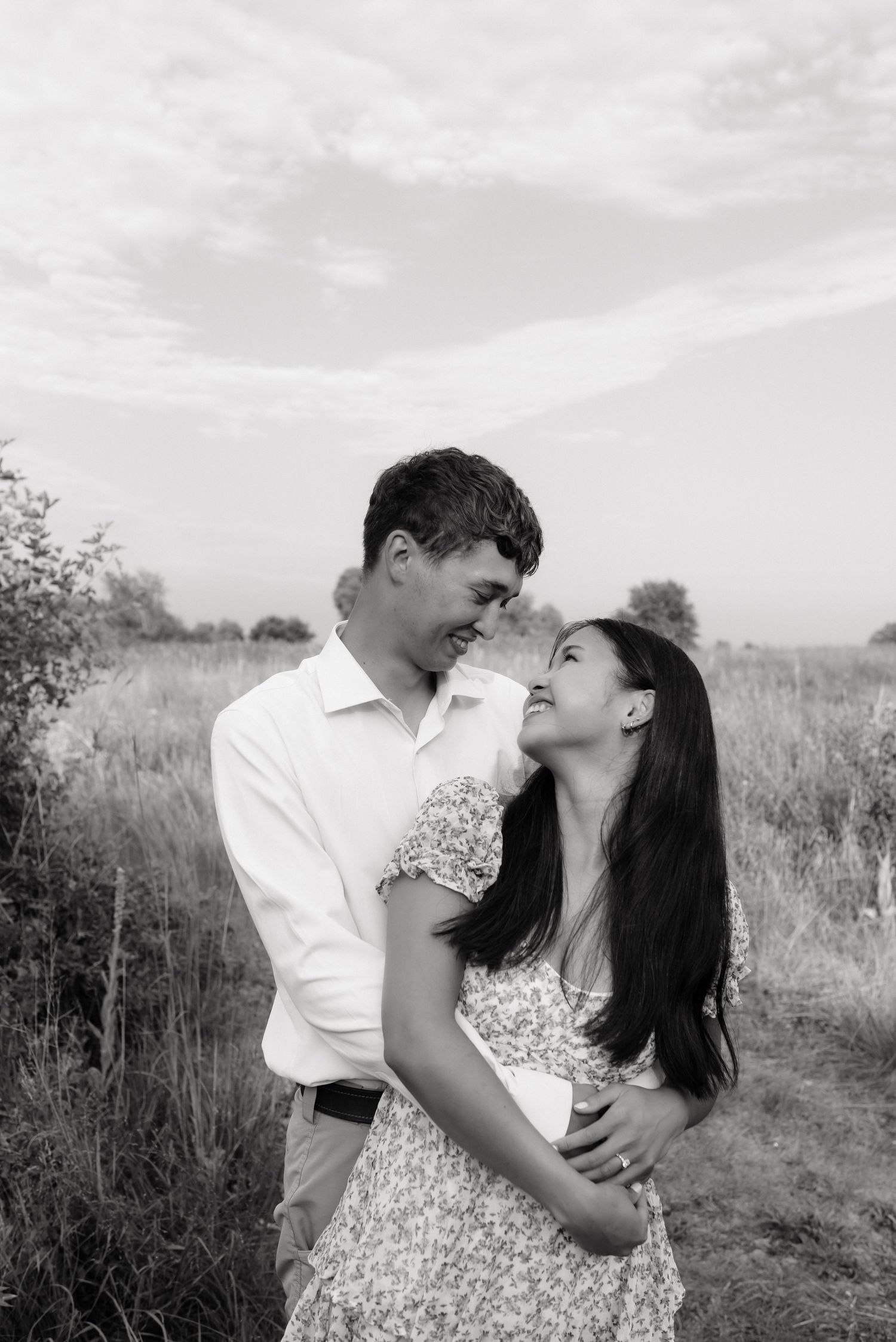 Black and white photo of a couple smiling and embracing in an open field.