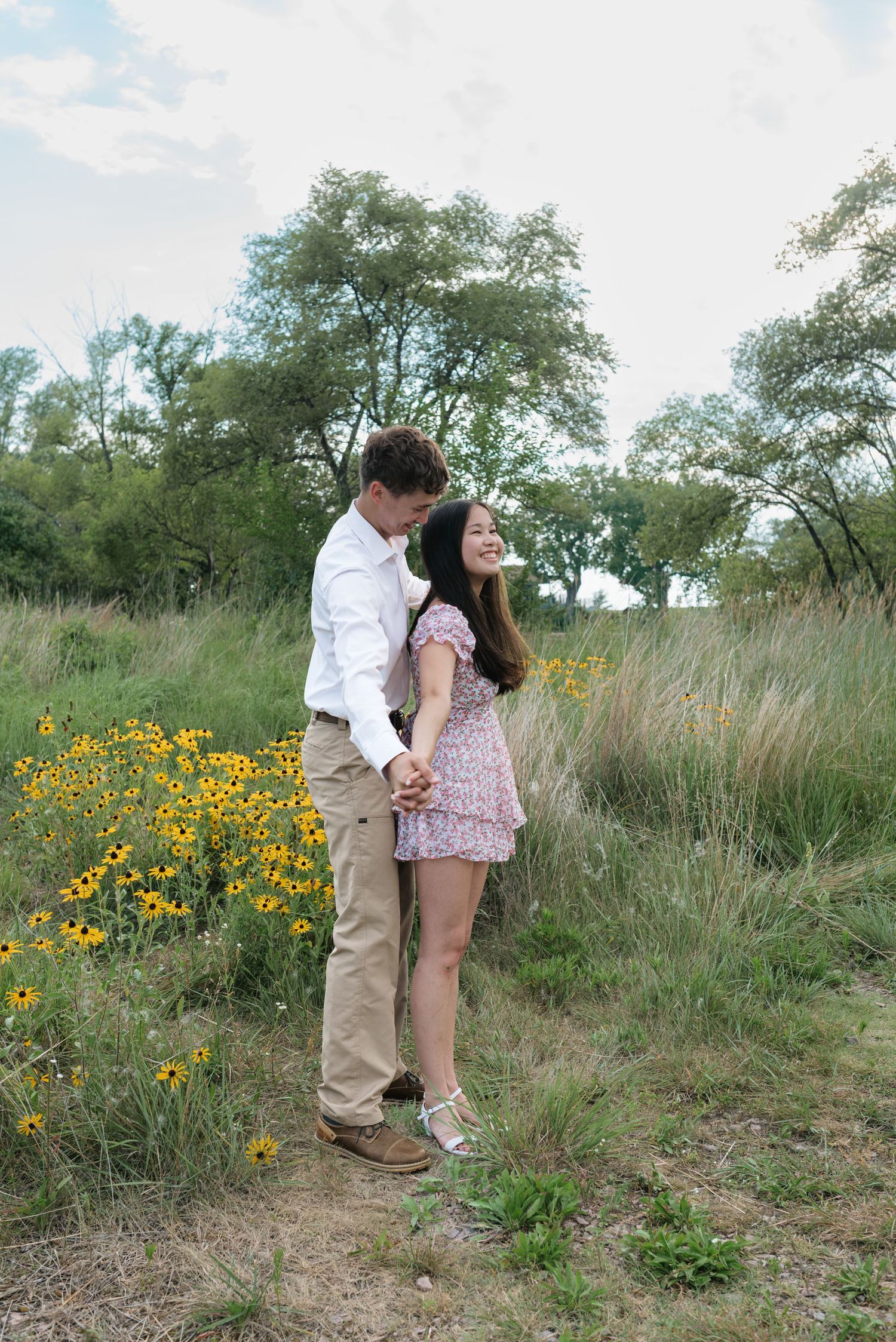 Young couple holding hands and sharing a tender moment on a nature path surrounded by yellow wildflowers.