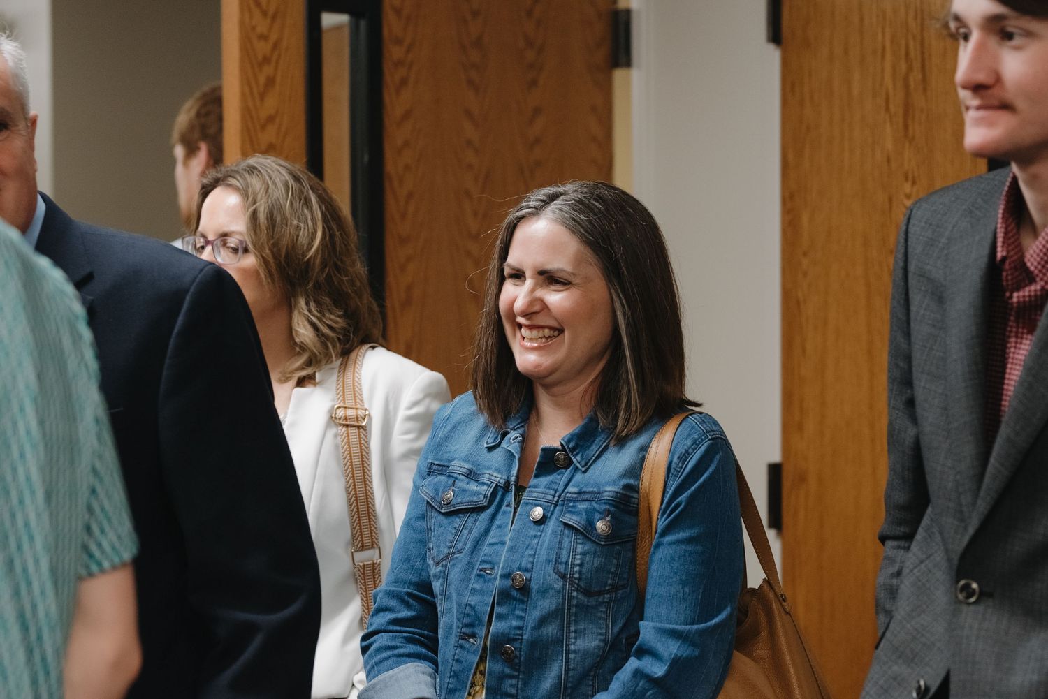 A smiling woman in a denim jacket mingles with guests at a wedding reception.