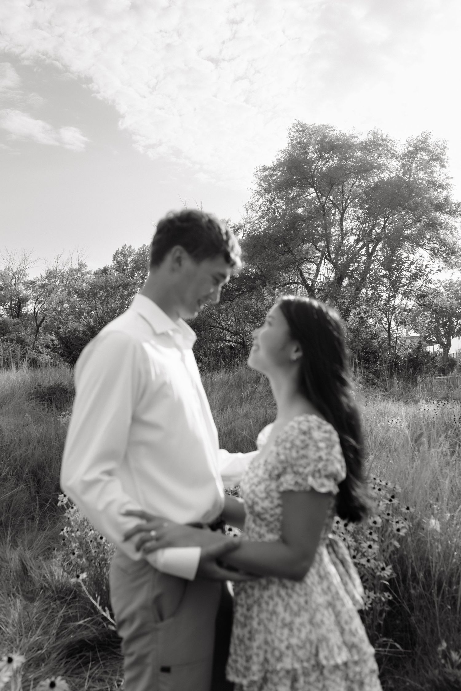Black and white photo of a couple holding hands and gazing at each other in a field.