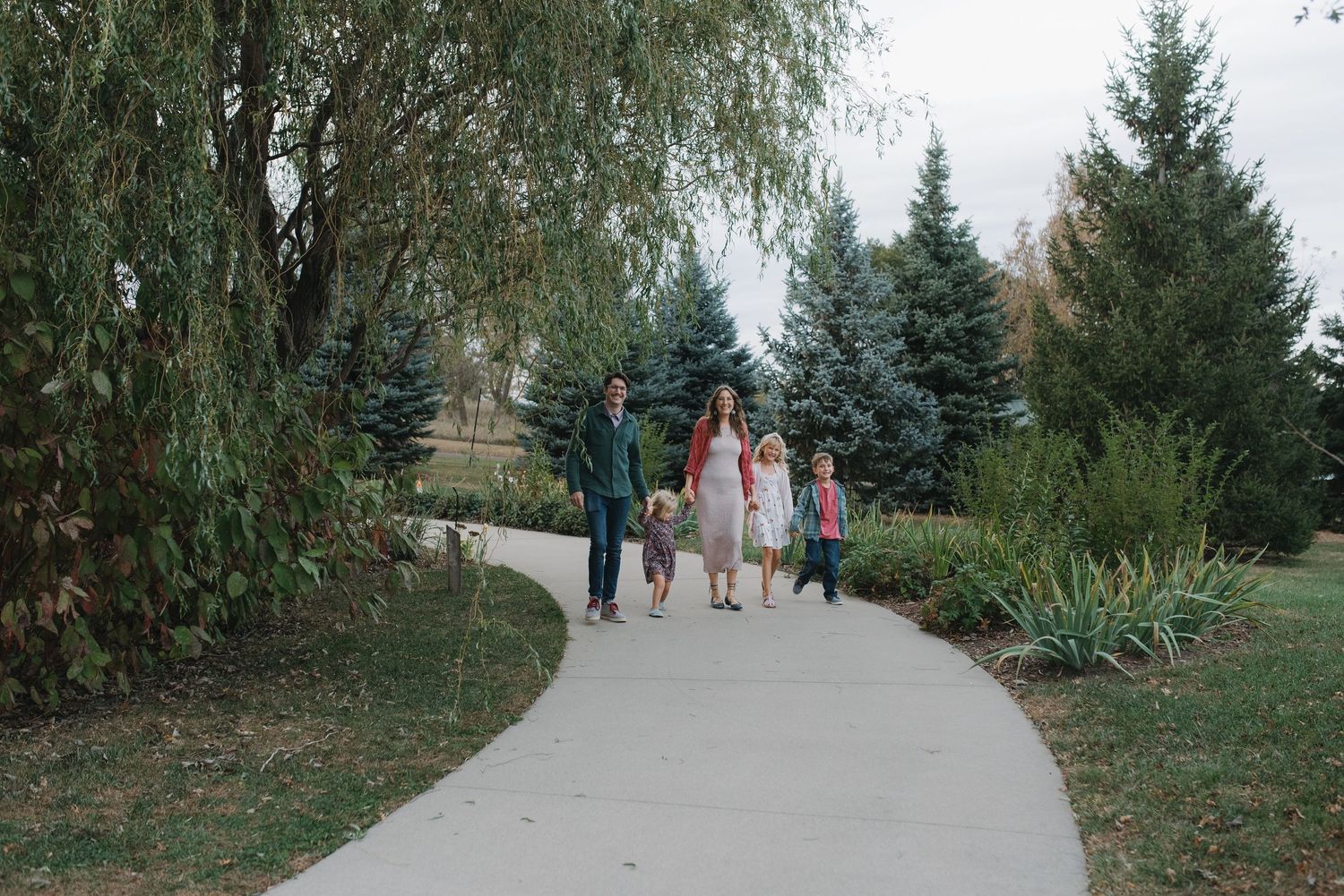 A family with two children walks along a scenic park path lined with trees.