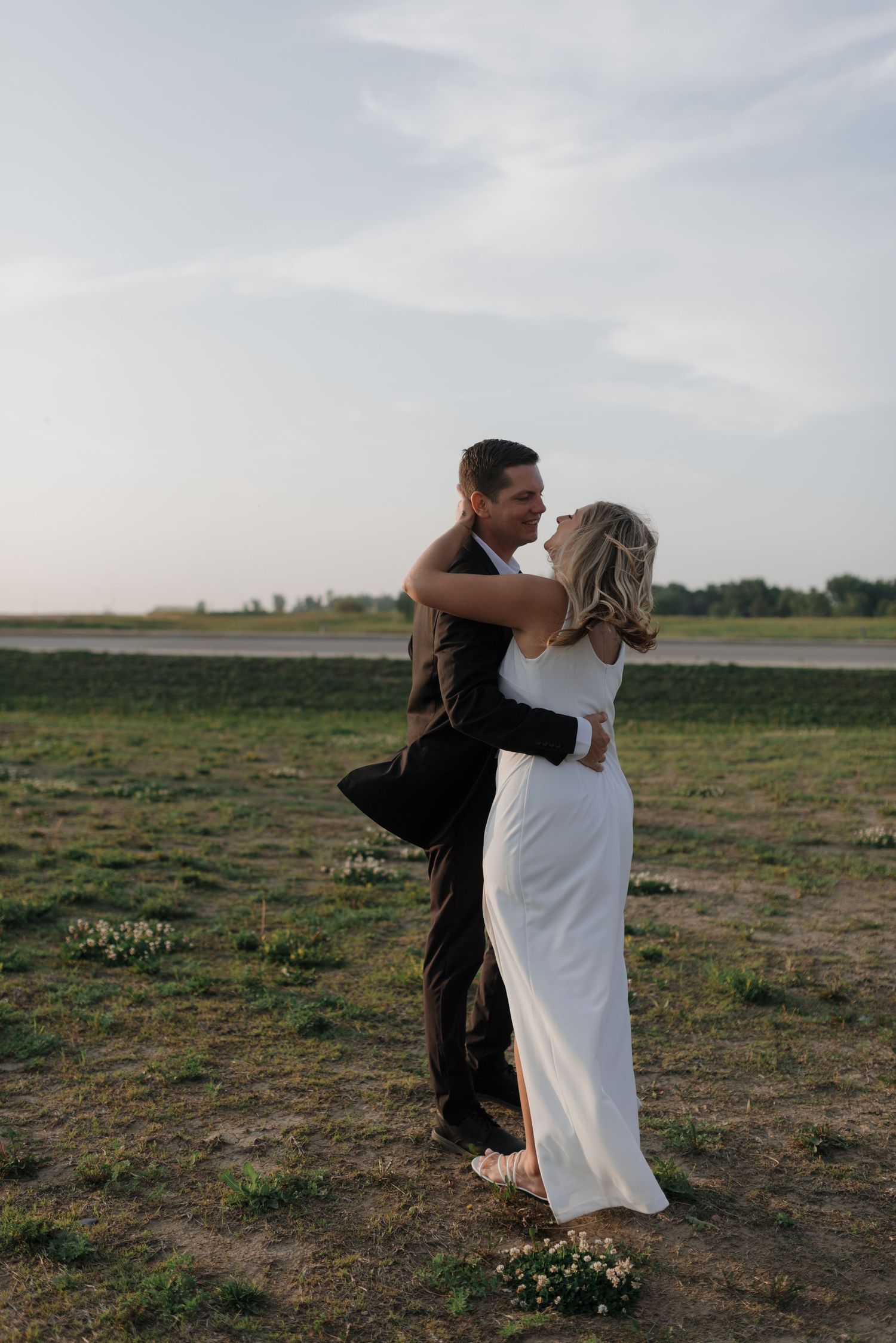 Bride and groom share a romantic moment gazing at each other in scenic outdoor field.