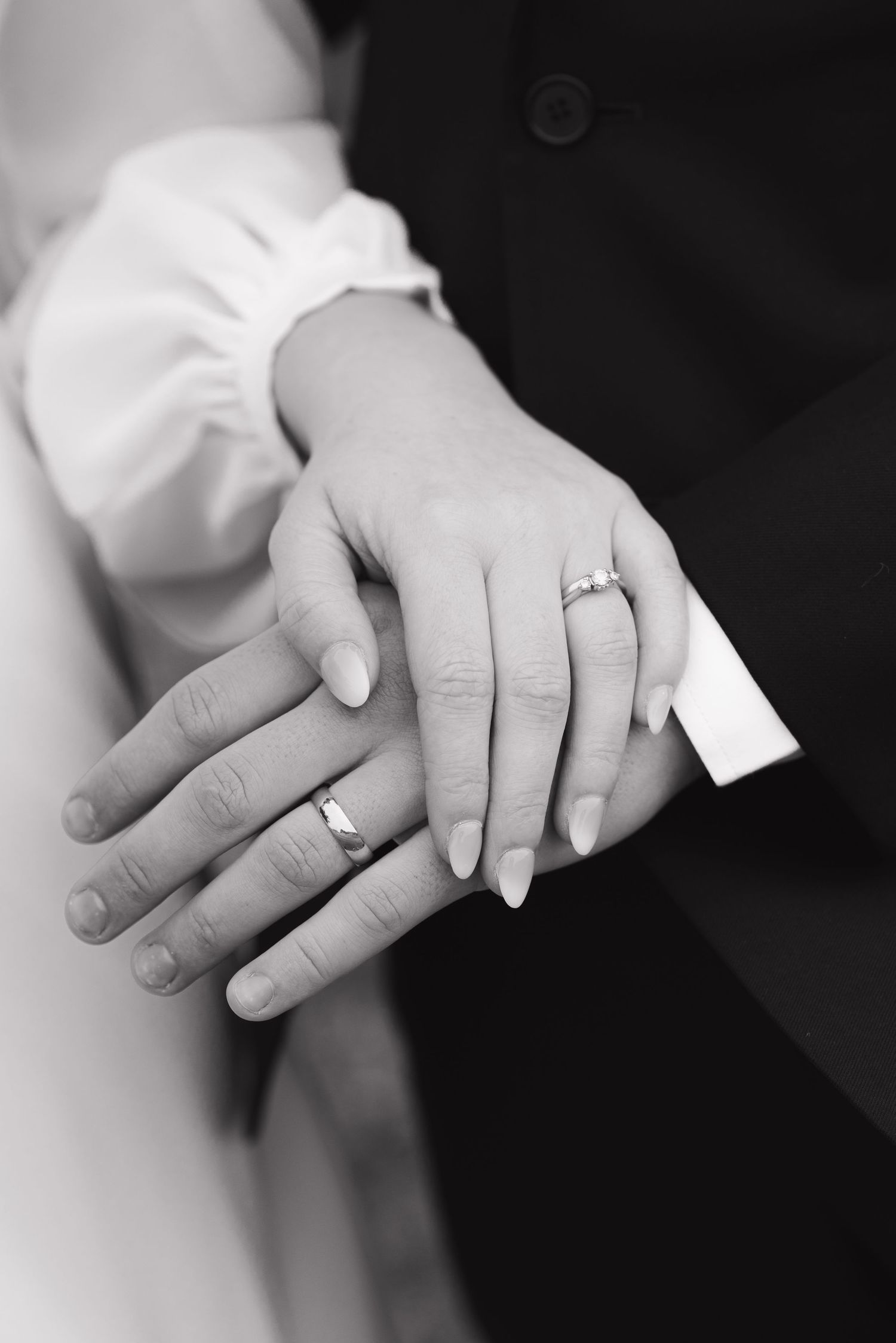 Newlyweds display wedding rings on joined hands in elegant black and white close-up photo.