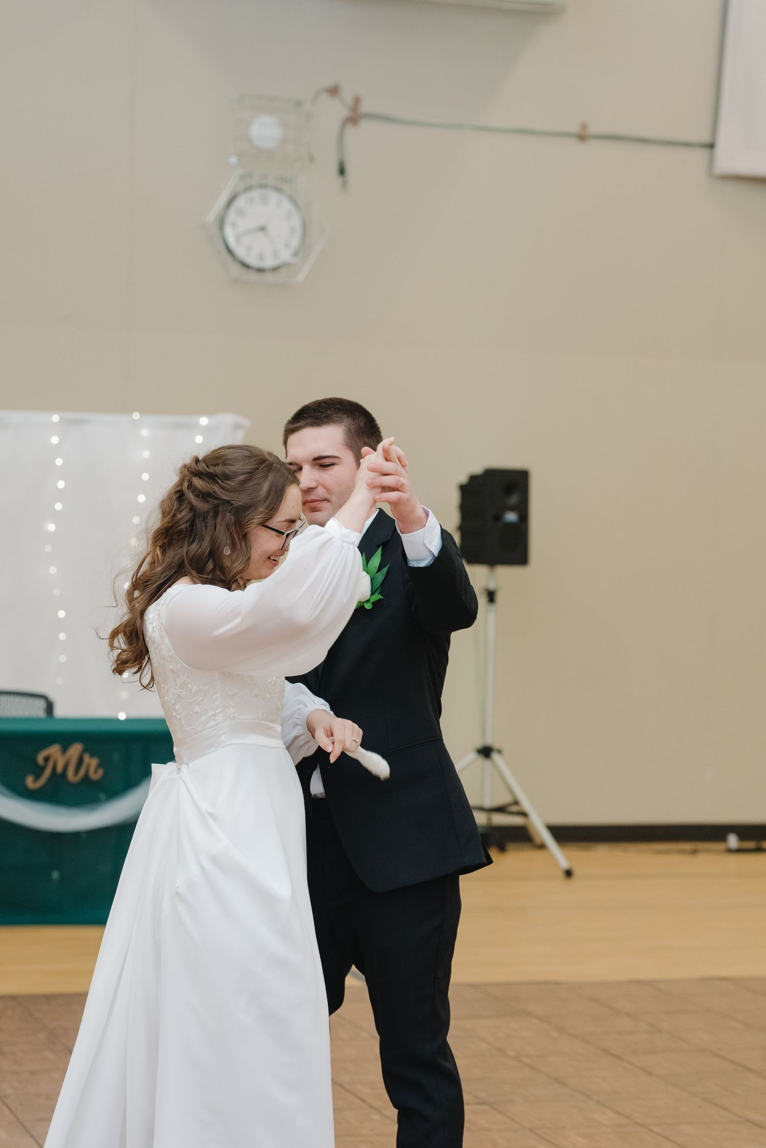 Bride and groom share their first dance in a decorated reception hall with string lights backdrop.
